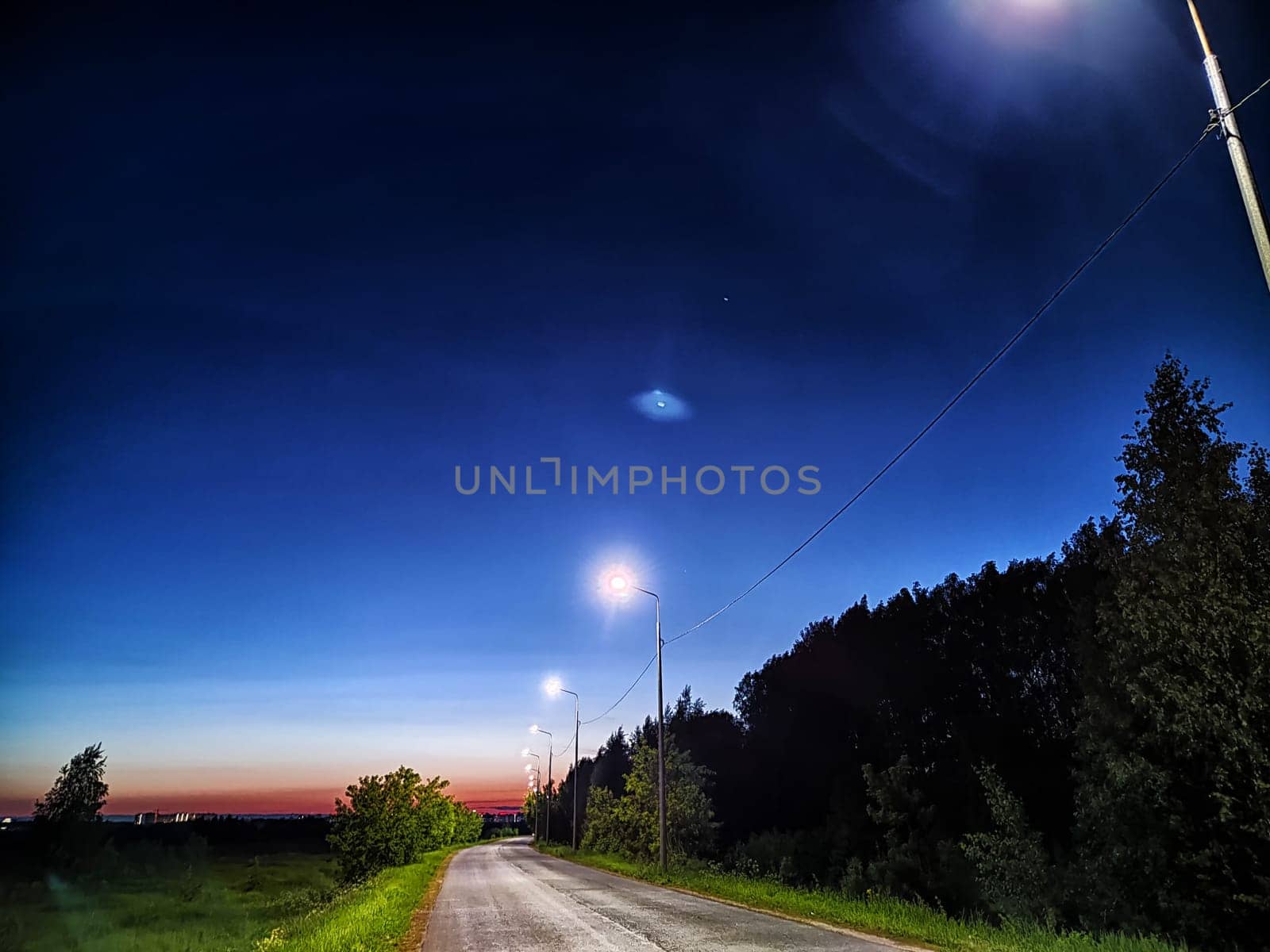 Asphalt road at night with lanterns on the side of road and the natural landscape around