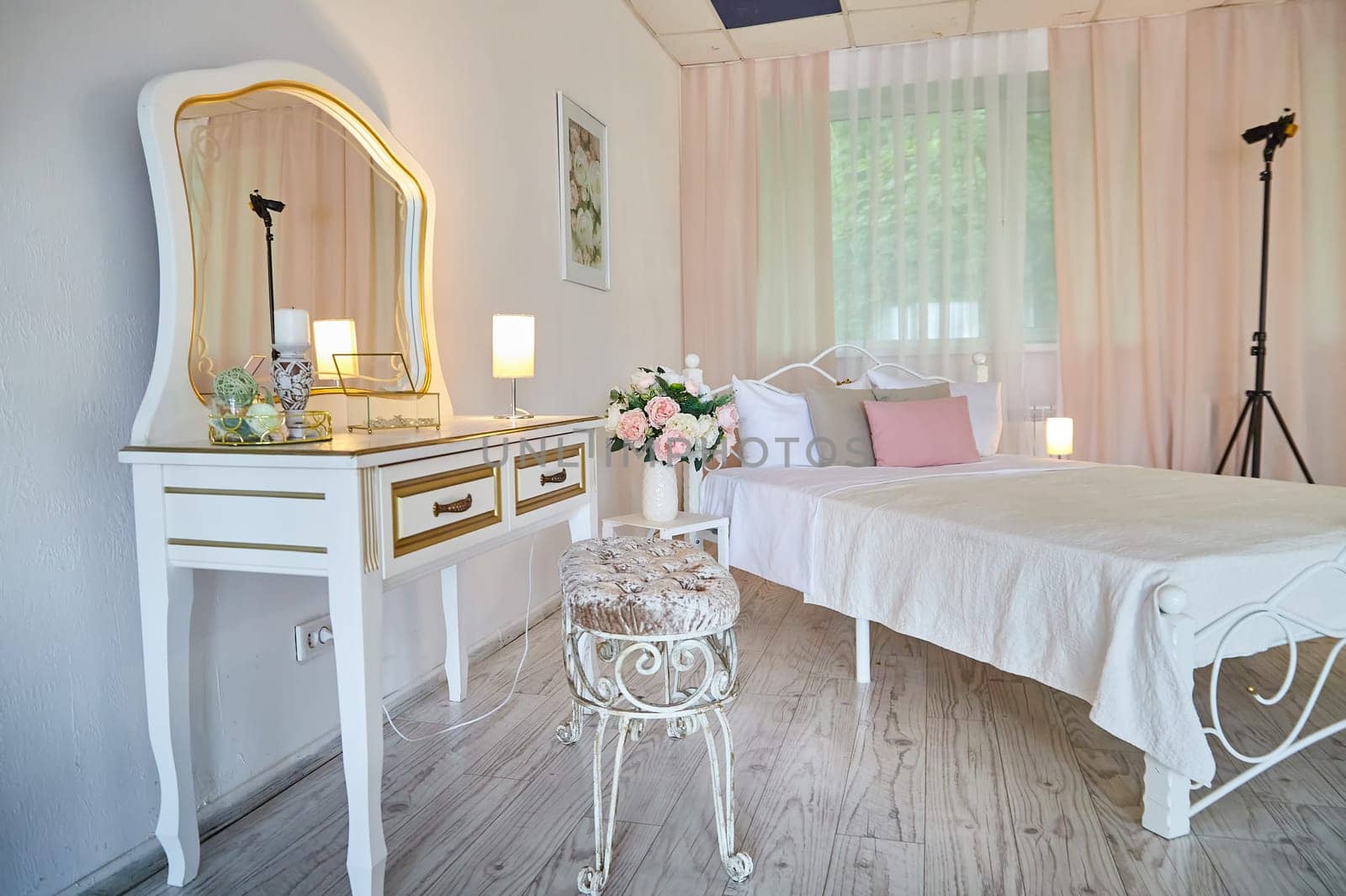 Cozy bedroom with bed located against mirror under dressing-table with lamp and window with curtain