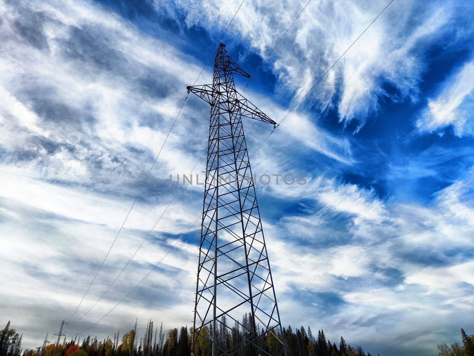Power lines on a hill, hill or in the mountains against a blue sky with white clouds. Electric lines, towers, wires in the landscape by keleny