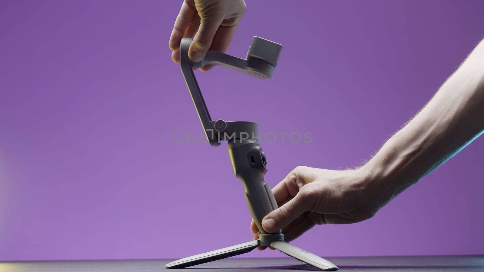 Portable video camera or smartphone electronic stabilizing system. Action. Close up of male hands setting professional equipment for shooting isolated on purple wall background
