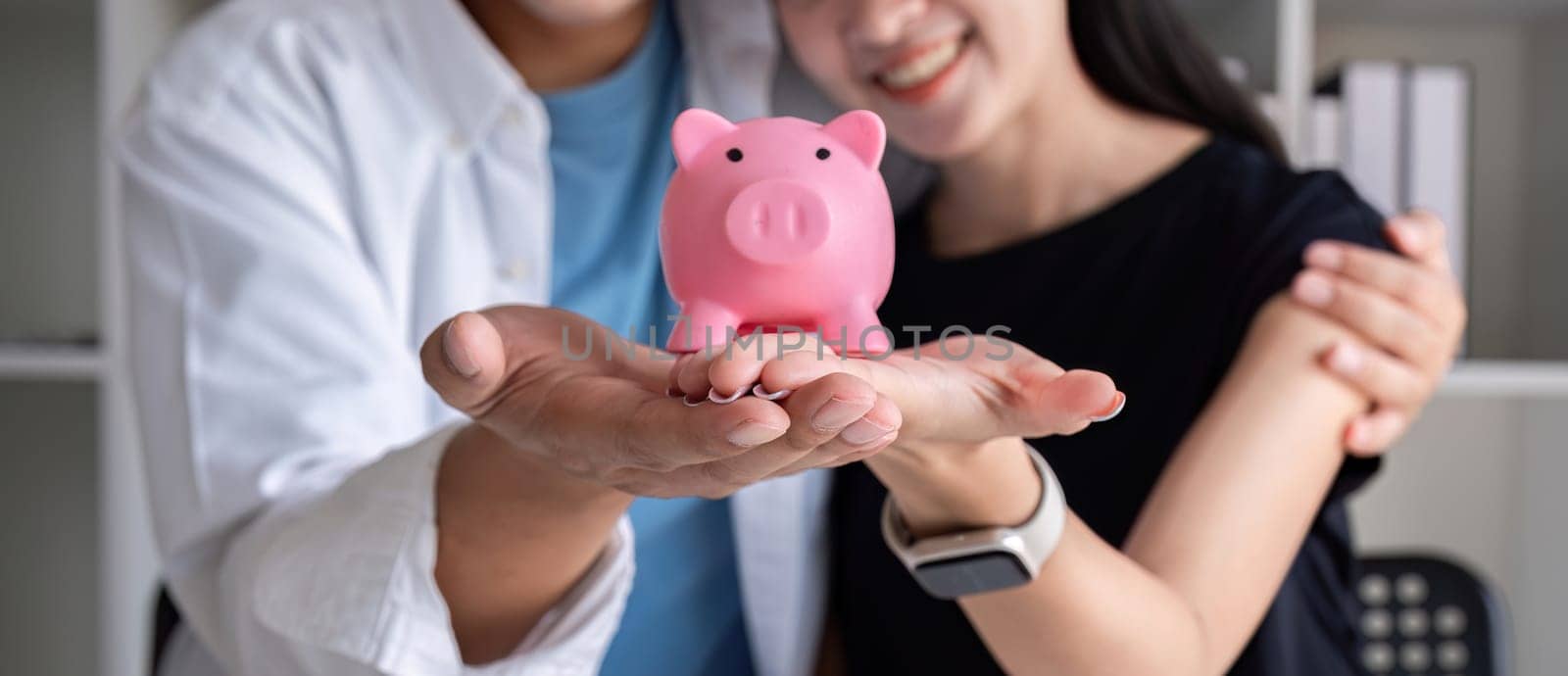 An Asian couple holds a pig model as a symbol of planning their savings together. by wichayada