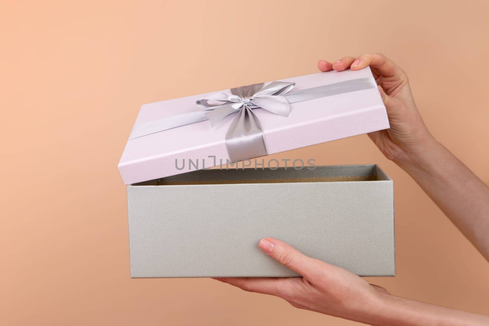 Side view of hands opening a box with a gift bow on a peach background by Demkat