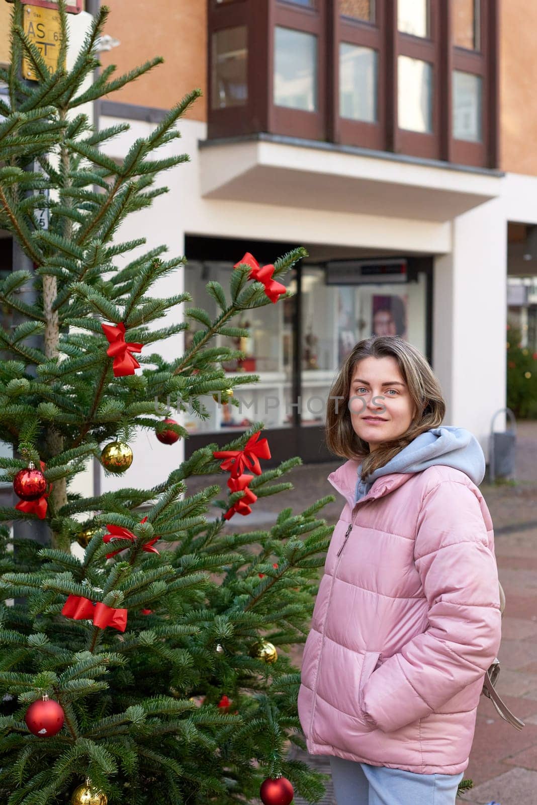 A beautiful girl stands on the street of the old European town of Bietigheim-Bissingen in Germany on Christmas Eve. City streets are decorated with Christmas trees and New Year's decorations, tourism, fashion, historical places, Europe by Andrii_Ko