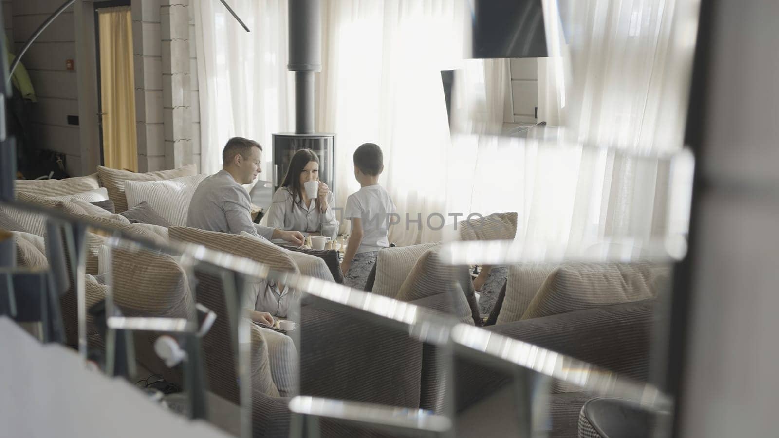 Rich family is eating in luxurious interior. Action. Parents with child rides in bright living room. Family of happy businessmen with child by Mediawhalestock