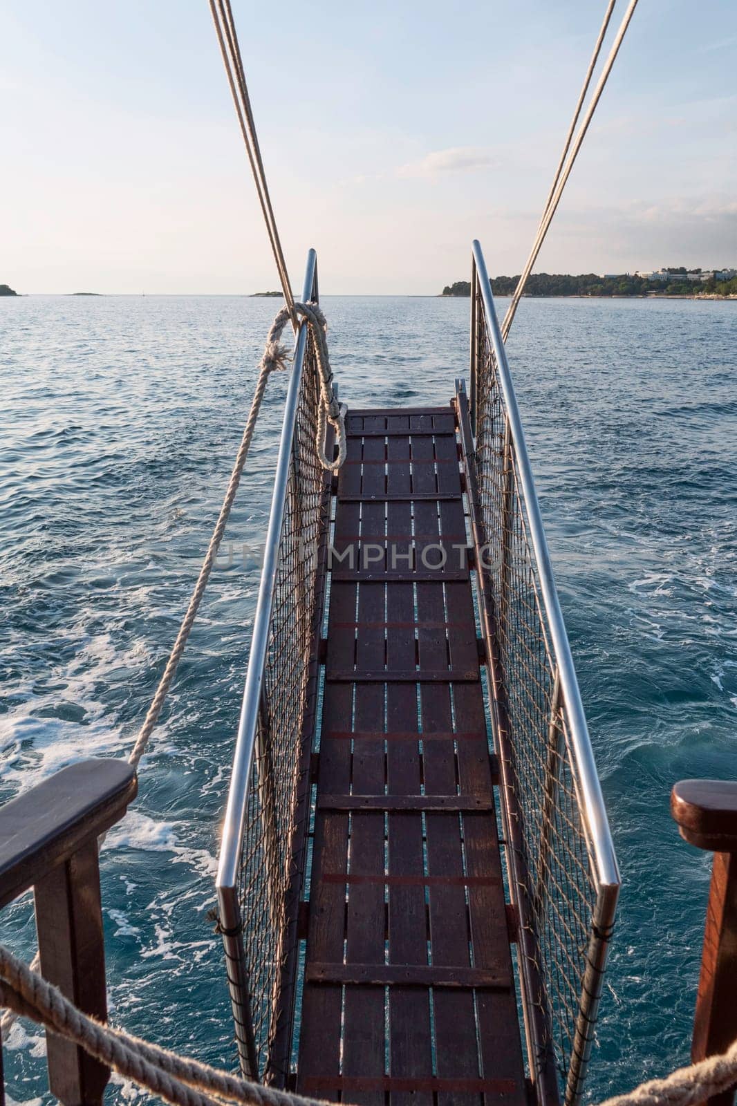 a brown wooden gangway with railing while sailing on the ocean by compuinfoto