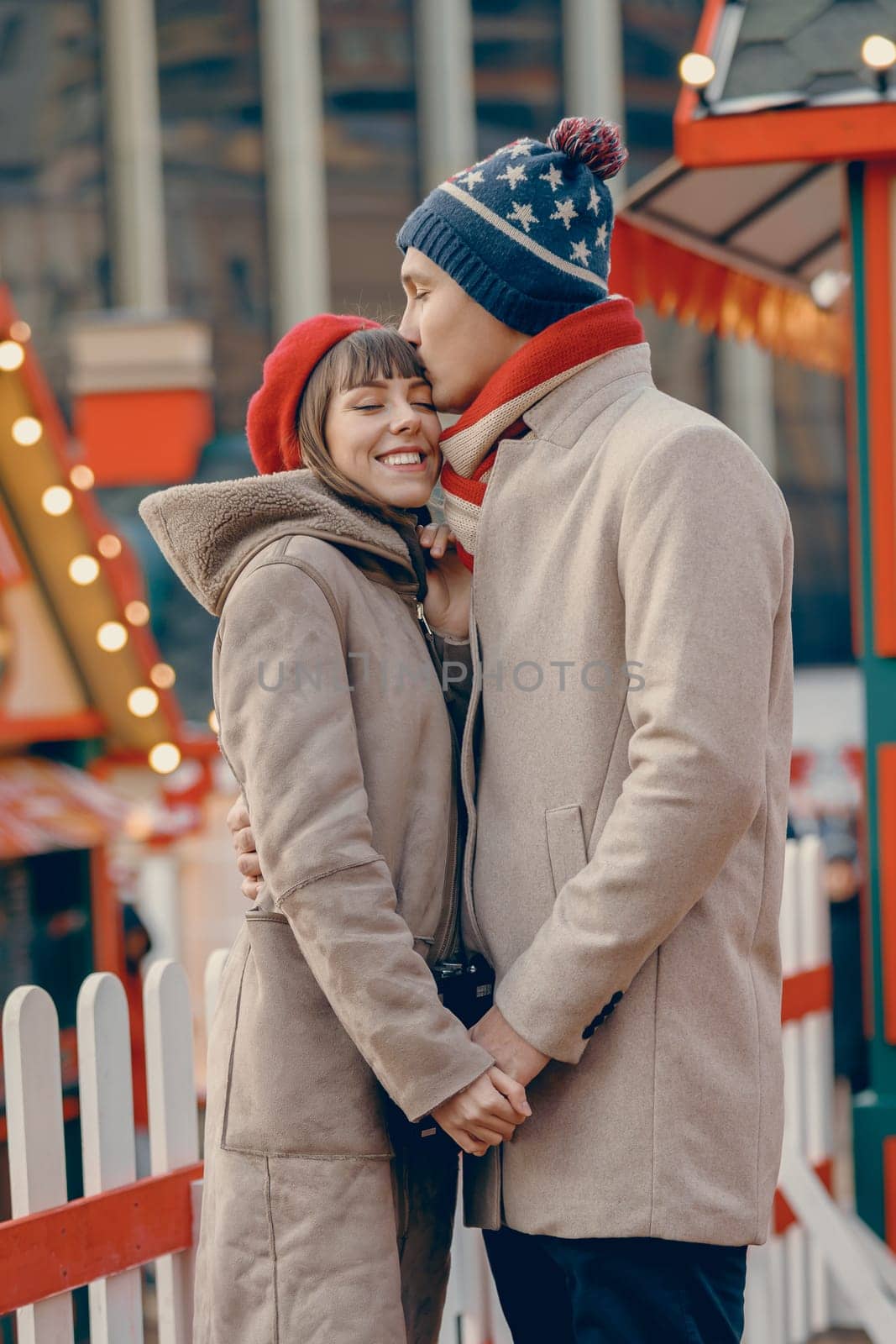 A heartfelt kiss between a couple is framed by the colorful and festive decor of a vibrant Christmas fair