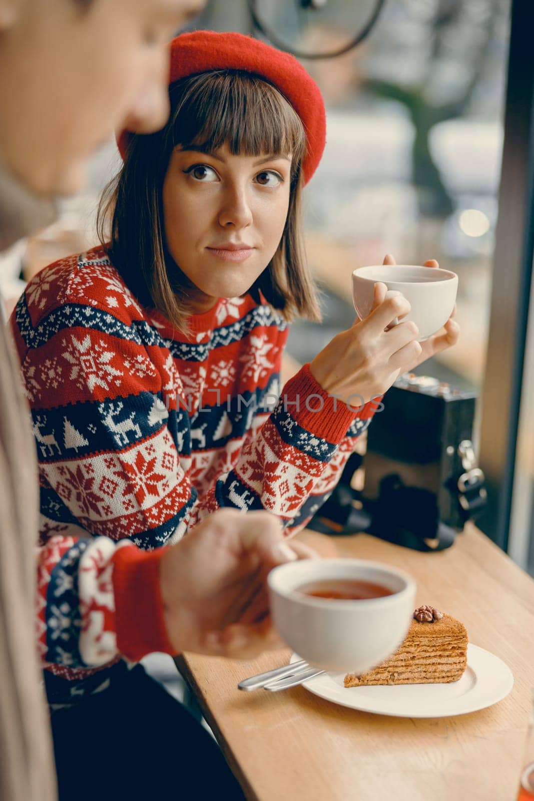 A contemplative moment as a young woman in a festive jumper enjoys a warm cup of tea, immersed in the coziness of a quaint cafe