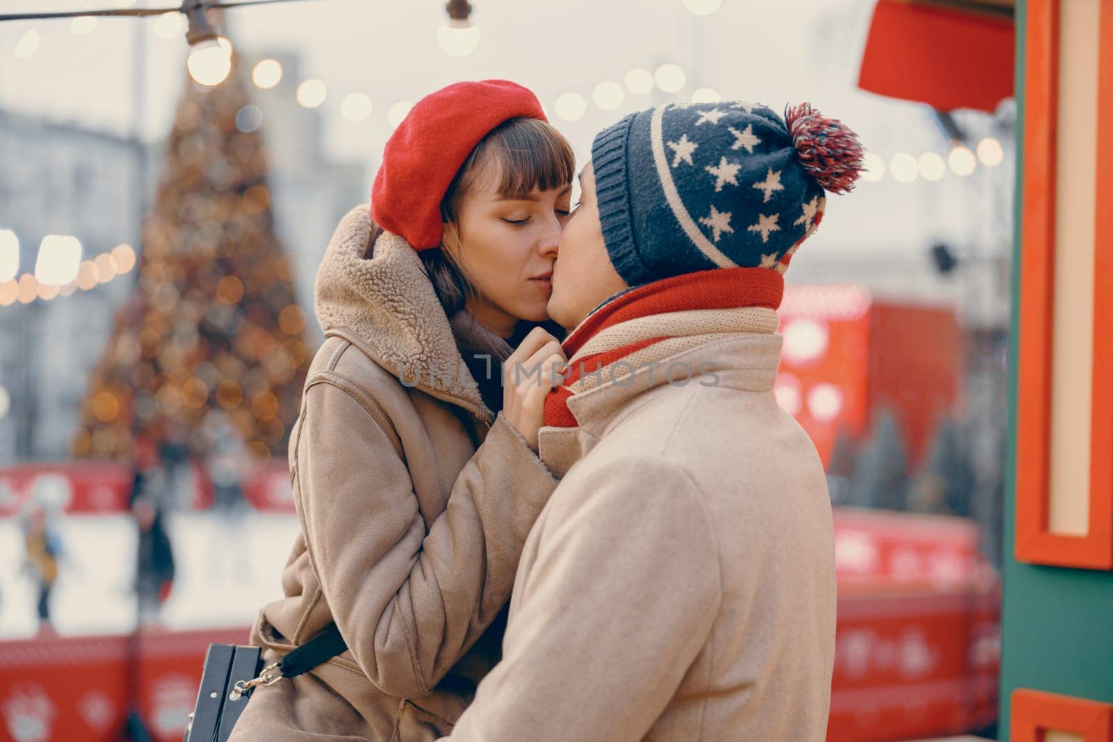 A romantic scene unfolds with a couple kissing gently amidst the twinkling lights of a holiday market, their winter attire adding warmth to the moment by Yaroslav_astakhov