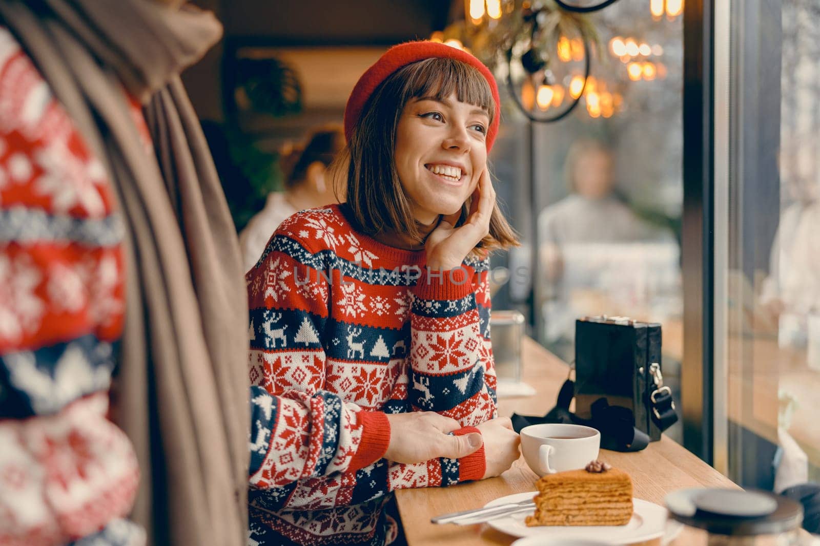Radiant young woman in a Christmas sweater shares a joyful moment at a cafe by Yaroslav_astakhov
