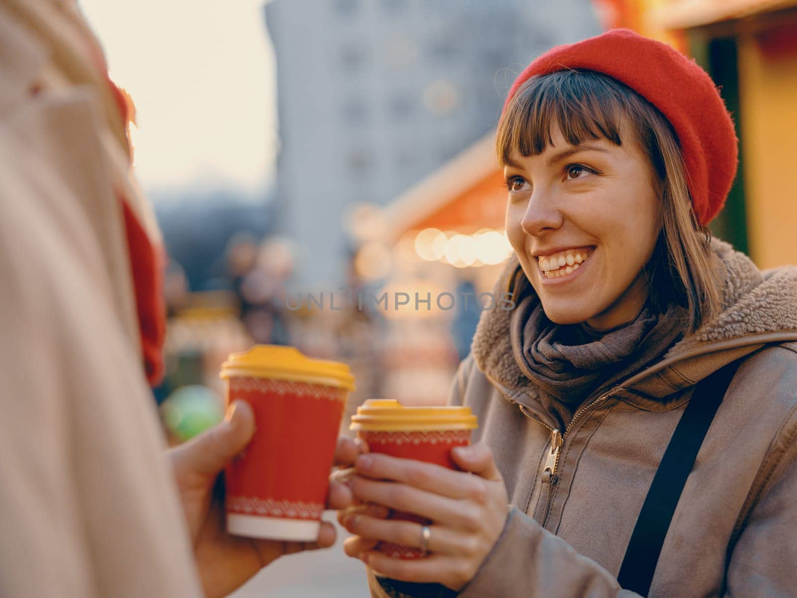A young woman beams at her partner, holding a seasonal drink, their shared happiness as warm as their festive beverages at the Christmas fair