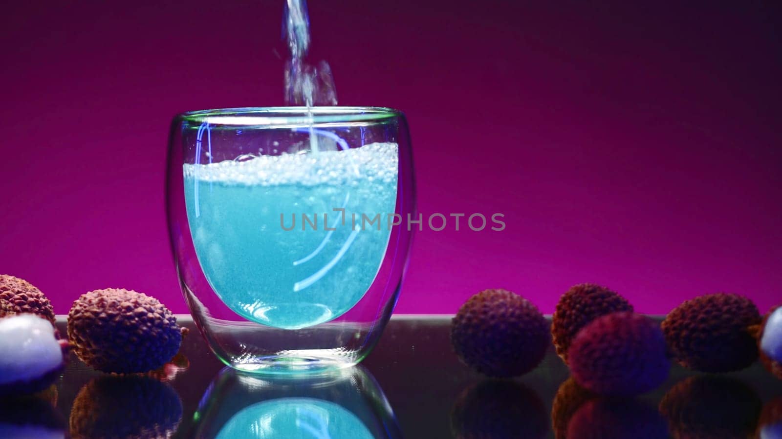 Blue drink is poured into glass on isolated background. Stock clip. Carbonated blue drink is poured into clear glass in bar. Bright drink with ingredients and fruits around.