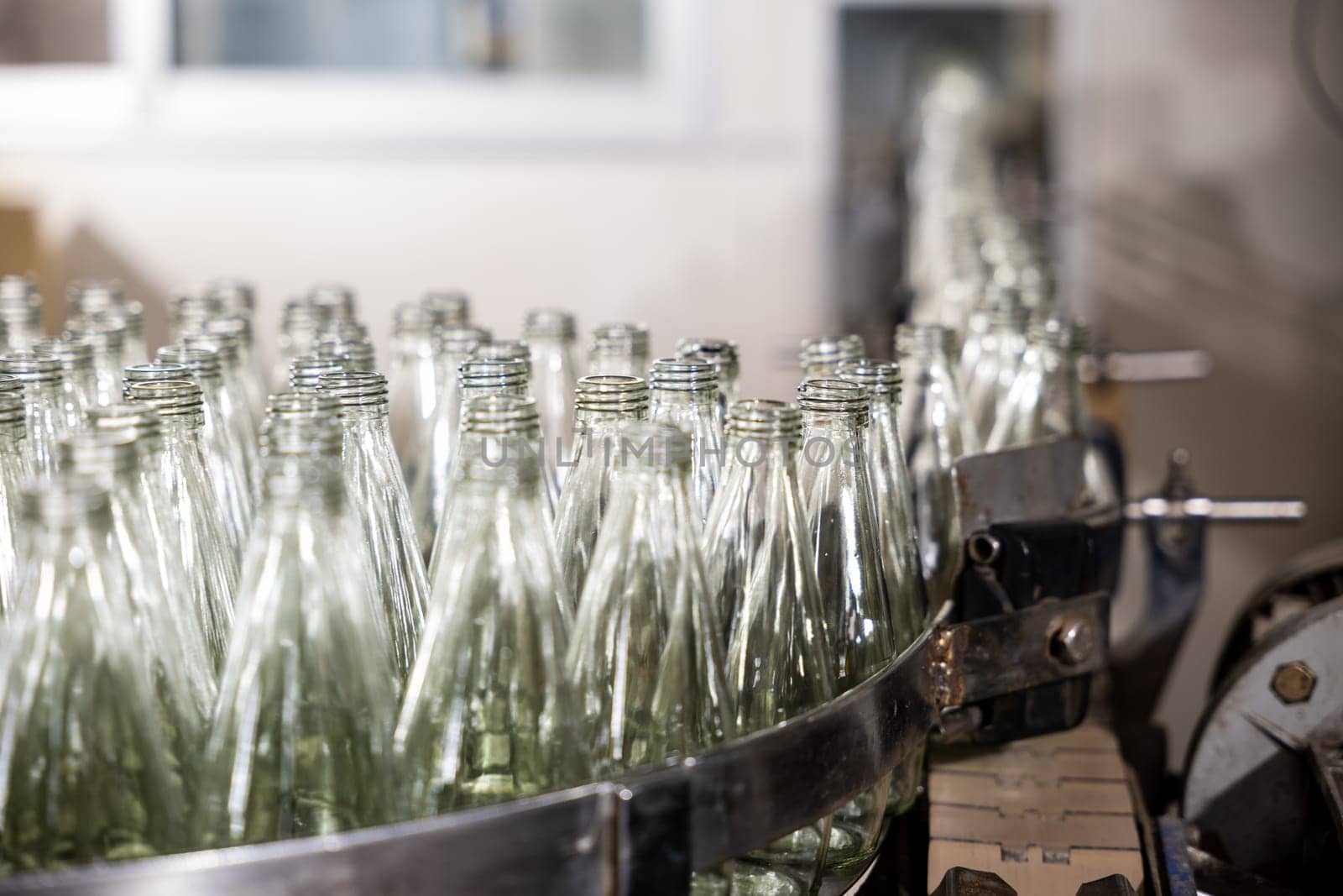 Empty glass bottles on a conveyor indicate a modern distillery's alcoholic beverage production and bottling by Sorapop