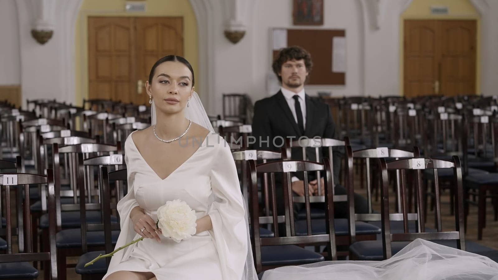 The wedding ceremony. Action.A huge hall with chairs where a young groom in a suit and a bride in a long white dress with a veil are getting married. High quality 4k footage