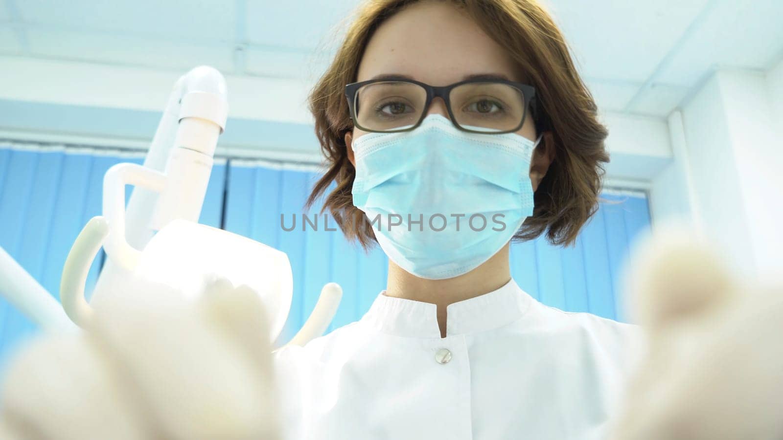 Bottom view of female dentist. Media. Attractive woman dentist with tools in hand treats teeth on background of dental electronic lamp.