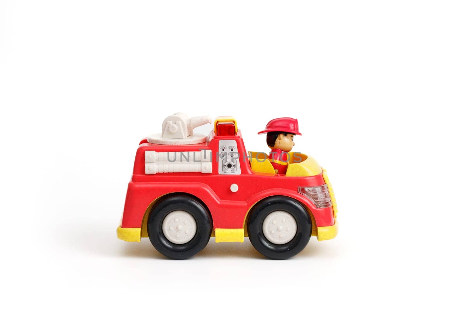 Kids toy plastic red fire truck with driver in the cabin, isolated on white background.