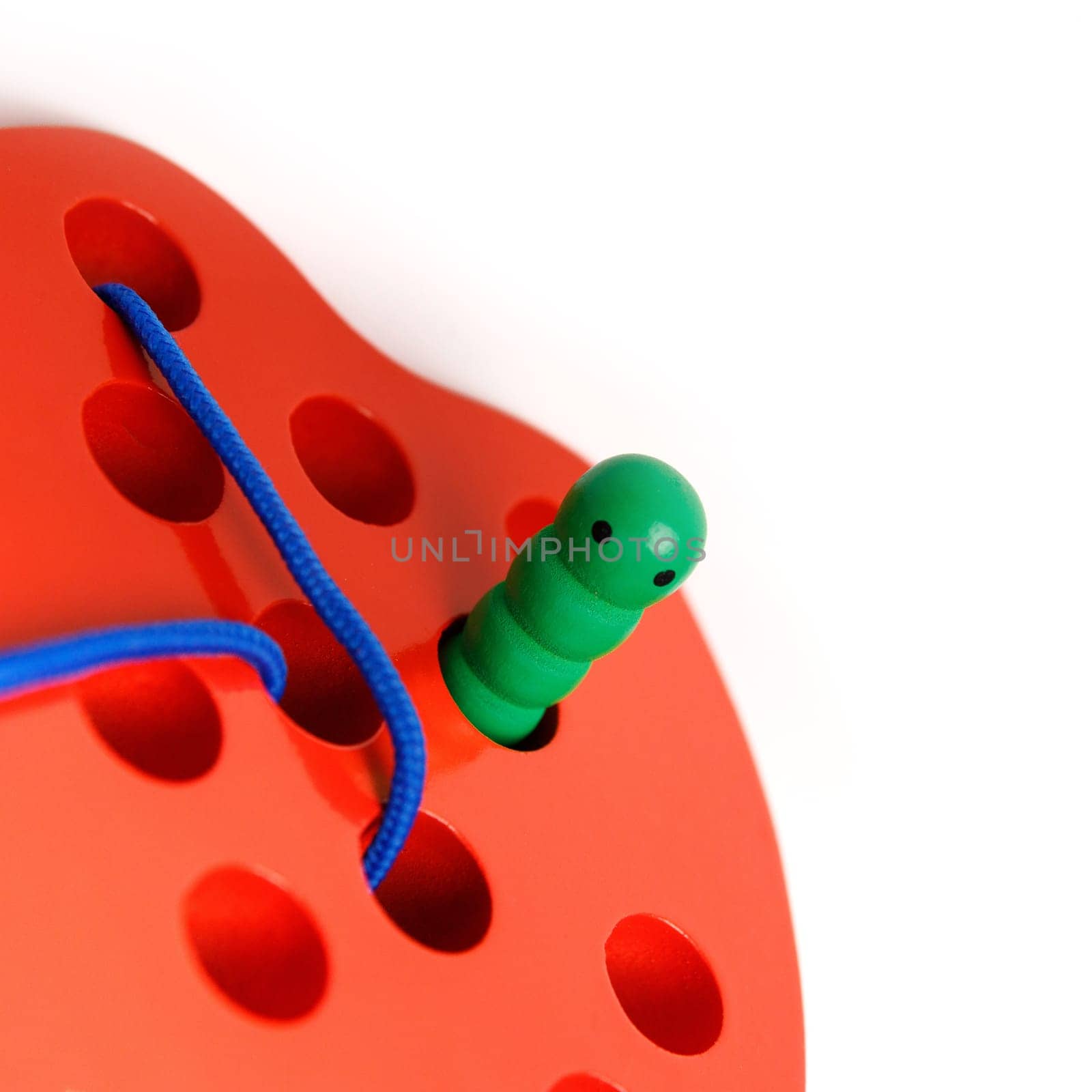 Kid's wooden toy in the shape of a red apple with a funny worm on a rope, toy for developing fine hand motor skills, copy space.