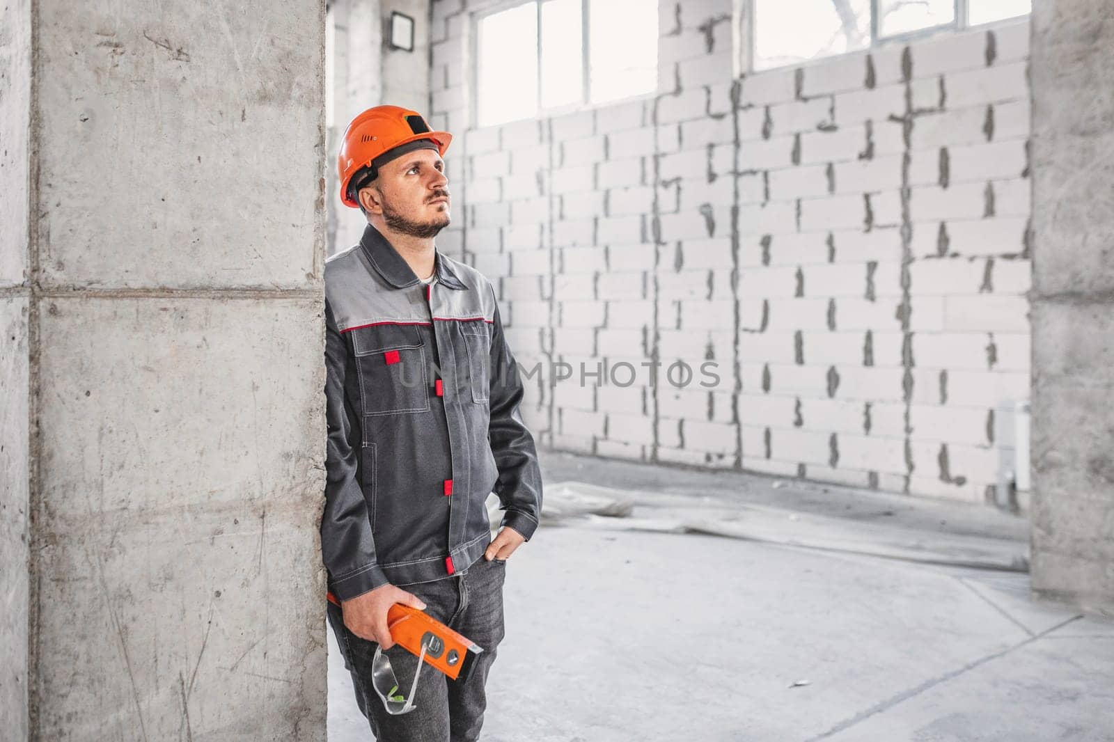 Portrait of a builder at a construction site near a reinforced concrete column, looking to the side, copy space.