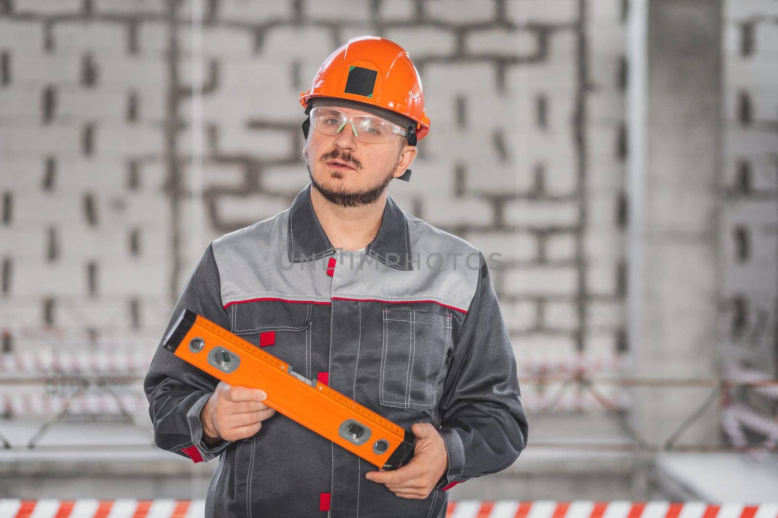 Portrait of a working foreman in a helmet with a level tool in his hands during an inspection of a construction site by Rom4ek