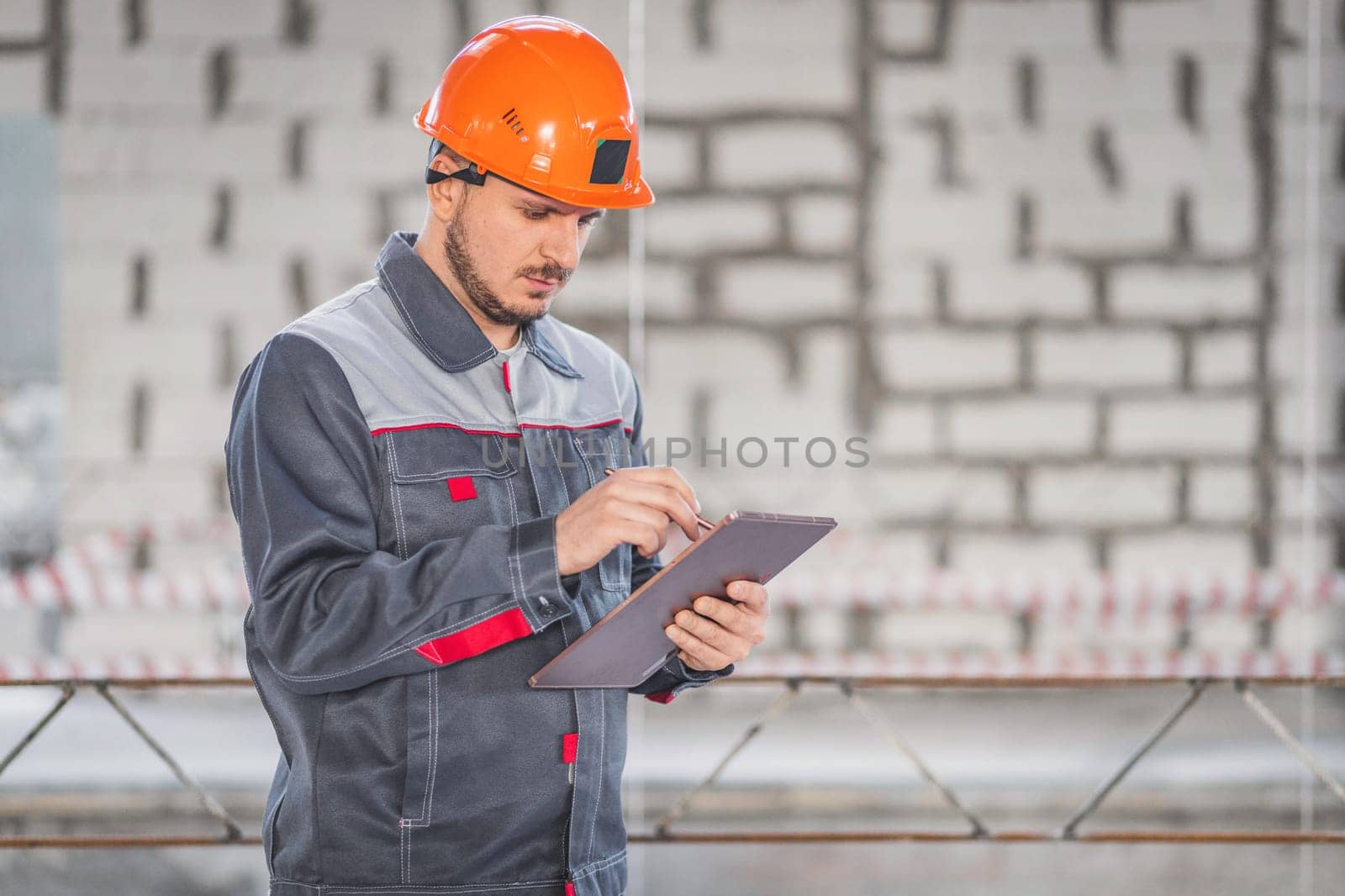 Caucasian construction worker in overalls and helmet using digital tablet on construction site, copy space by Rom4ek