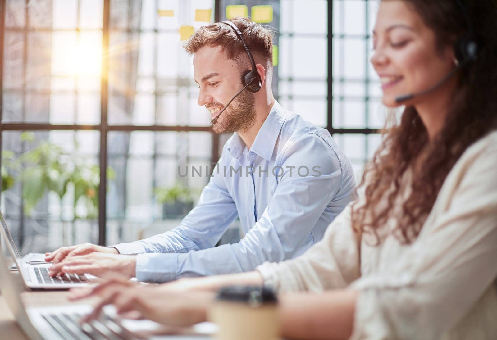 male call-center operator with headphones sitting at modern office, consulting online information in a laptop, looking up information in a file in order to be of assistance to the client.