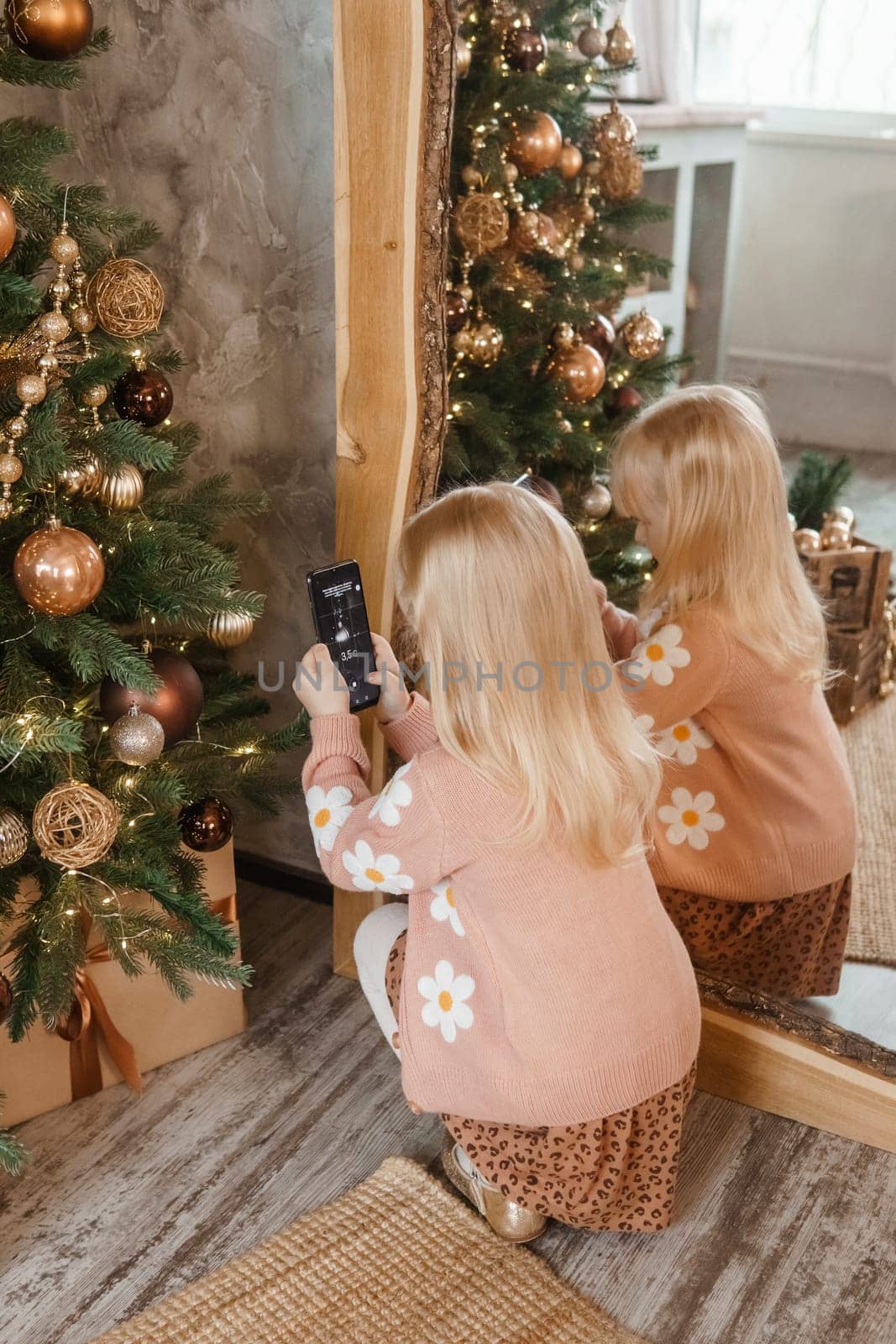 A little blonde girl photographs balloons on a Christmas tree in a festive interior decorated in a New Year's style. The concept of a merry Christmas