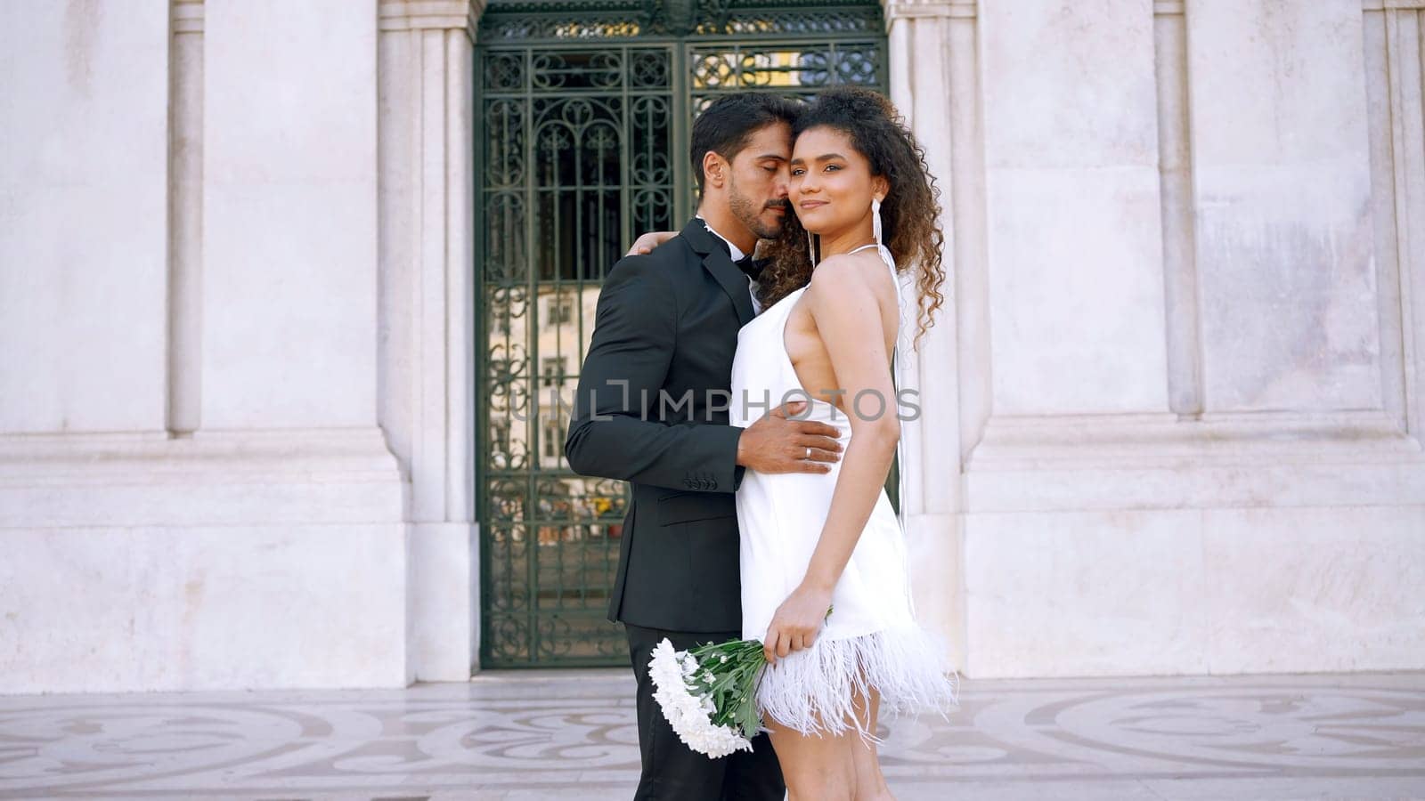 Beautiful couple in outfits happily embracing. Action. Attractive couple in luxurious outfits on street of old town. Gorgeous young couple happily embraces on sunny day.