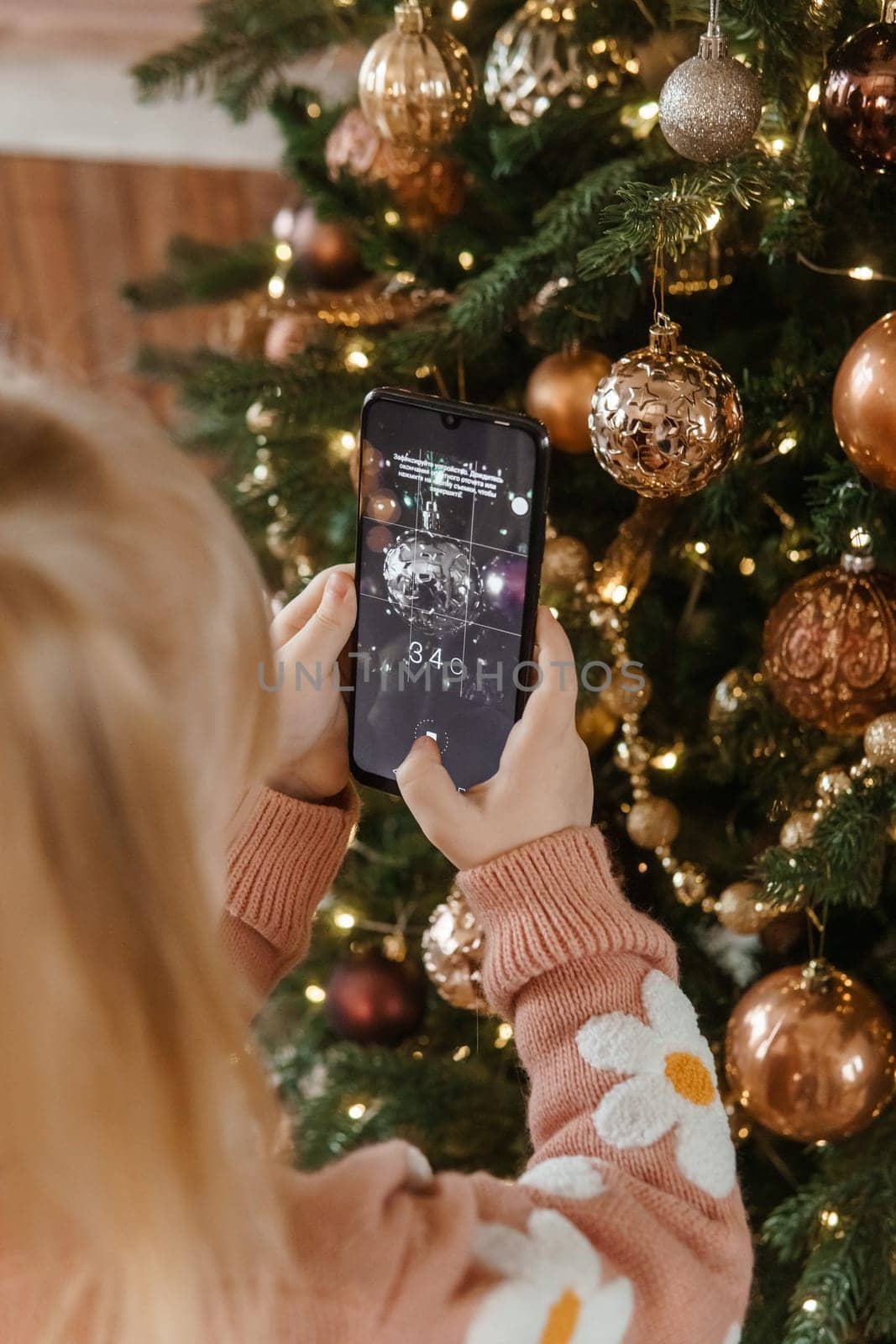 A little blonde girl photographs balloons on a Christmas tree in a festive interior decorated in a New Year's style. The concept of a merry Christmas