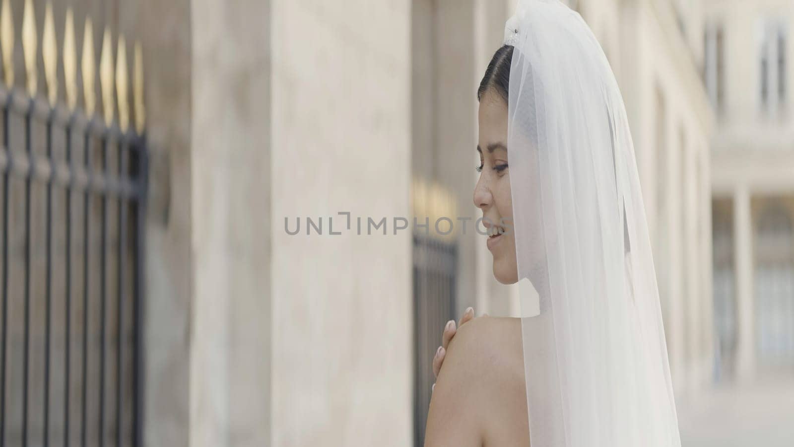 Portrait of seductive young bride in wedding dress and luxury veil poses for camera near metal fence. Action. Concept of wedding and starting family