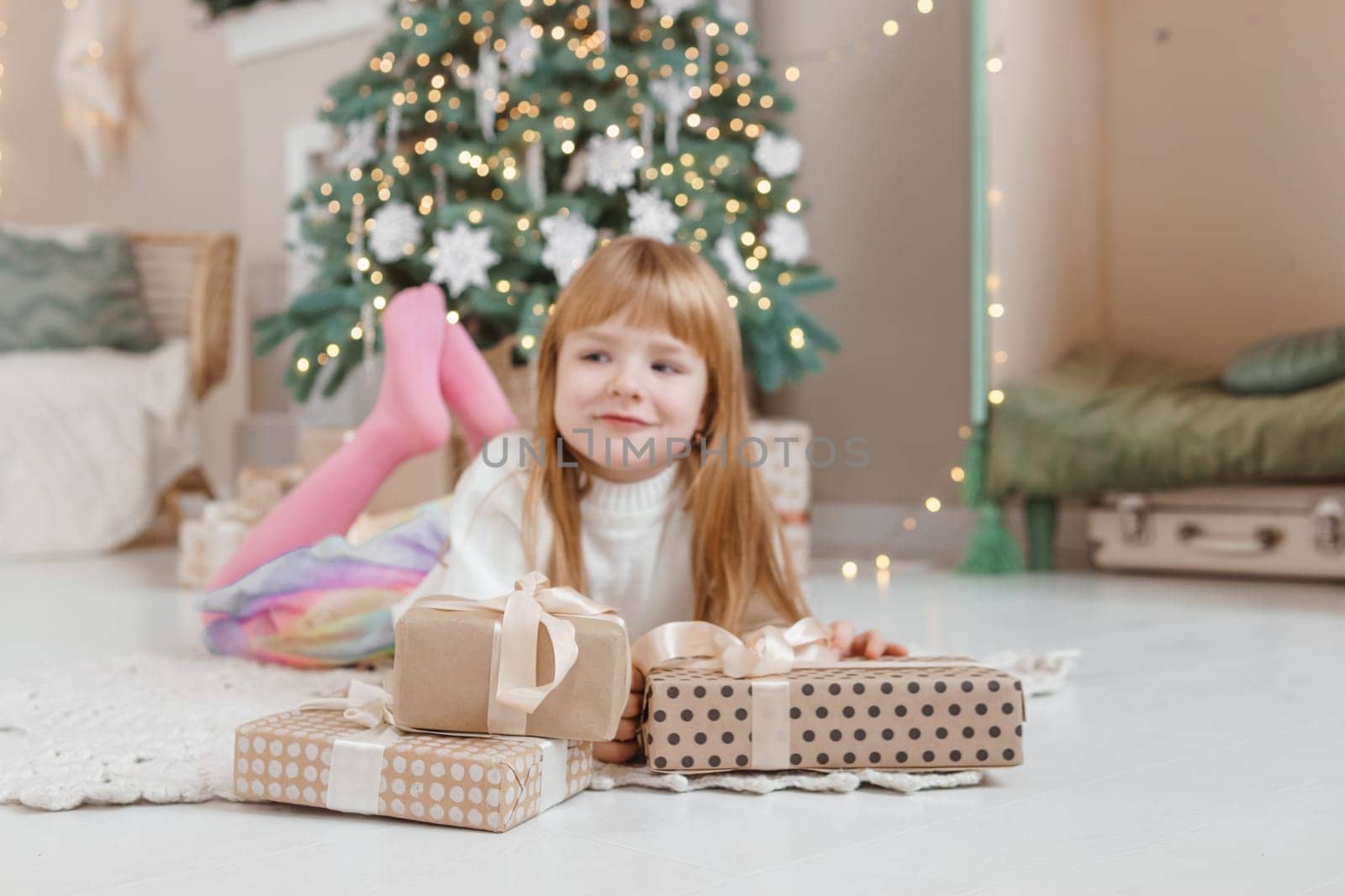 A little red-haired girl lies next to Christmas gifts in a craft package. Happy Christmas concept