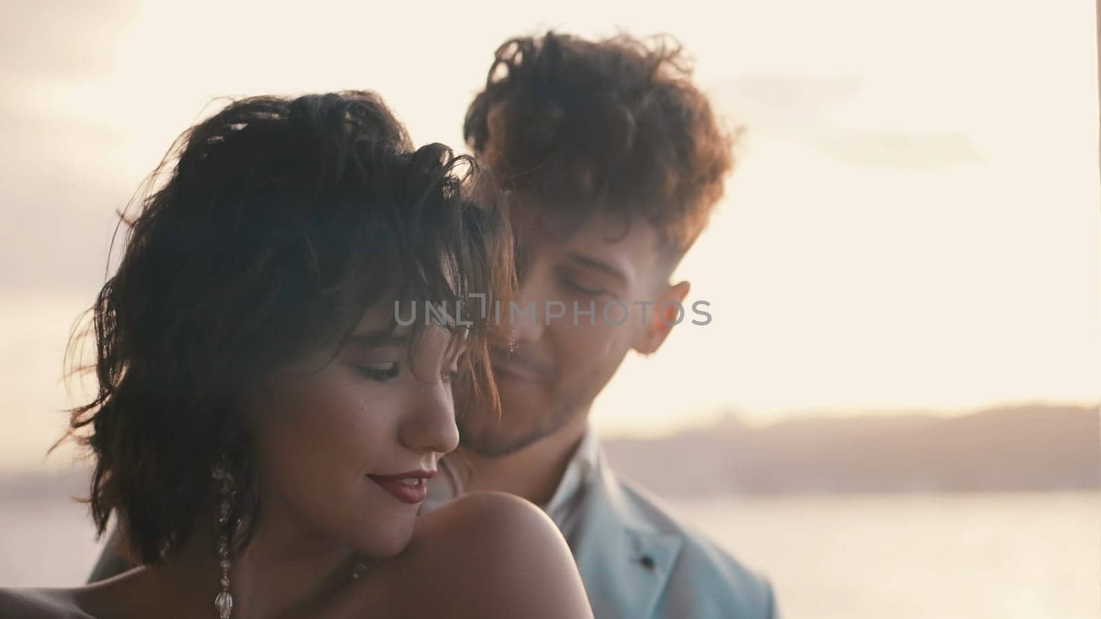 Beautiful stylish couple on sunny background. Action. Attractive newlyweds stand on blurry background with the sun. Stylish and elegant couple of newlyweds.