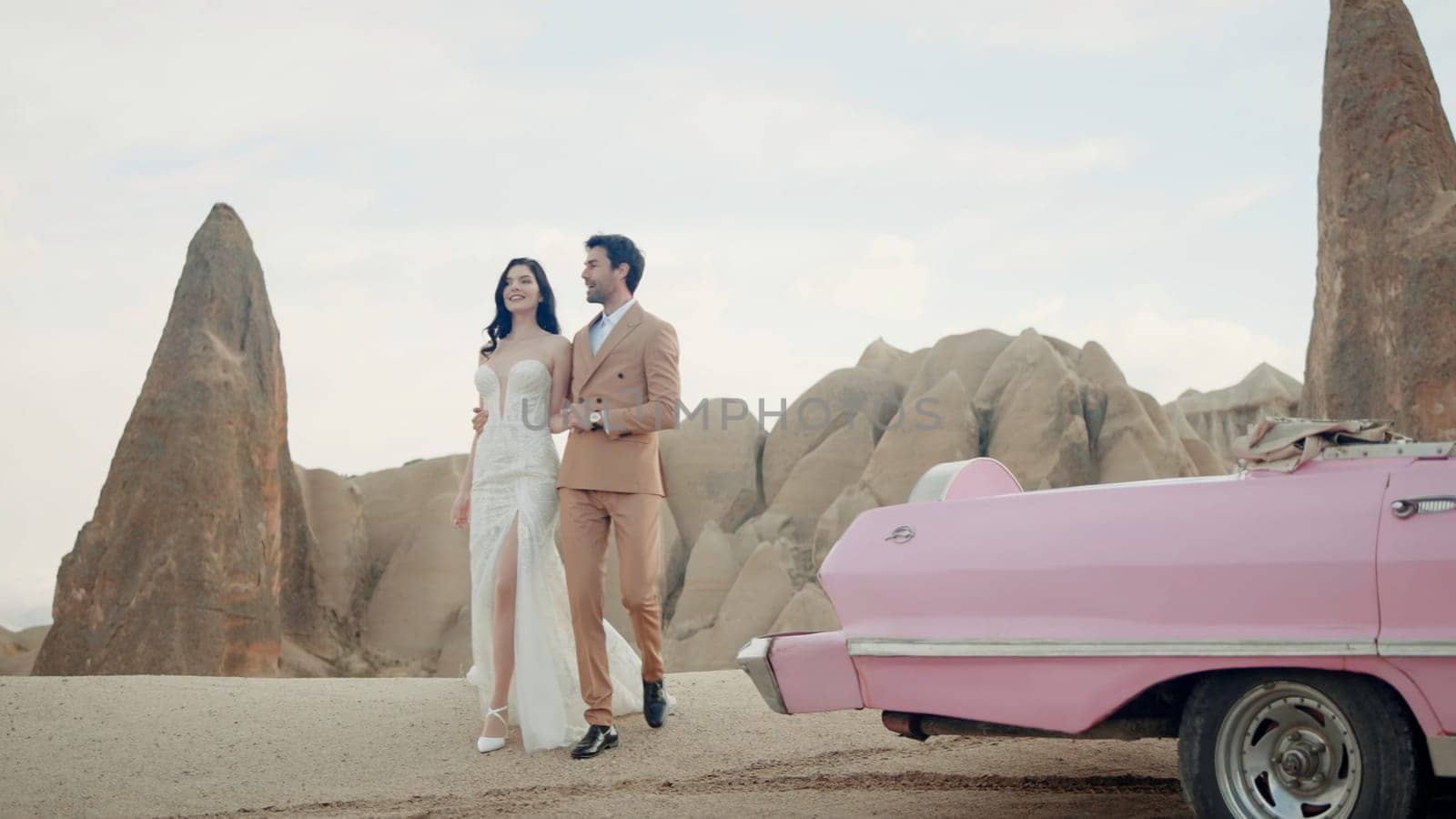 Beautiful young couple during photo session on the top of a mountain in Cappadocia. Action. Romantic love of man and woman couple near the cabriolet pink car