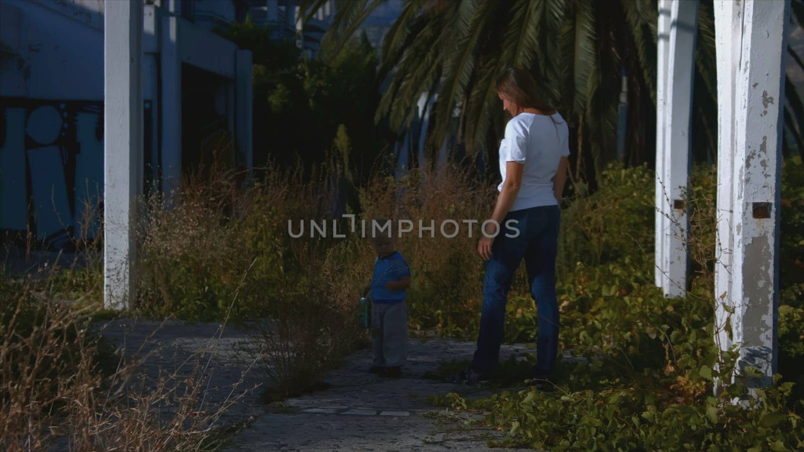 Woman follows child on walk in summer. Creative. Woman stands with child and watches him on walk. Woman walks with child in nature in summer in sunny day.