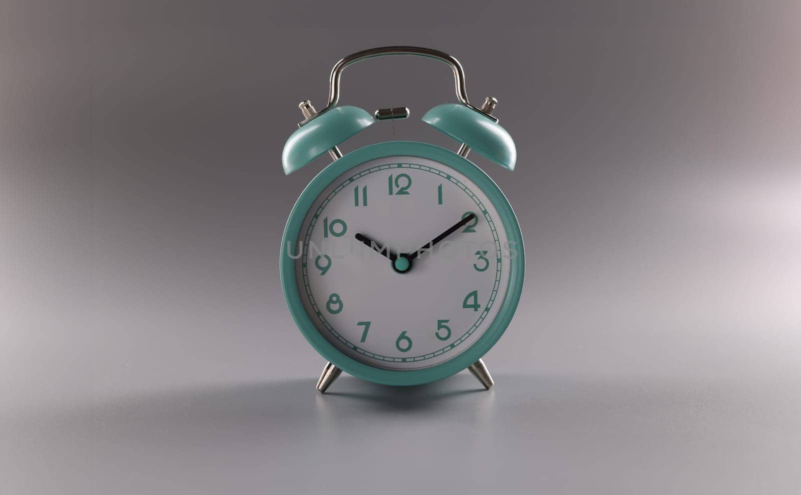 Close-up of single simple designed green retro clock on grey surface. Metal vintage clock on tiny legs stand. Time, timer, alarm, decor, rarity concept