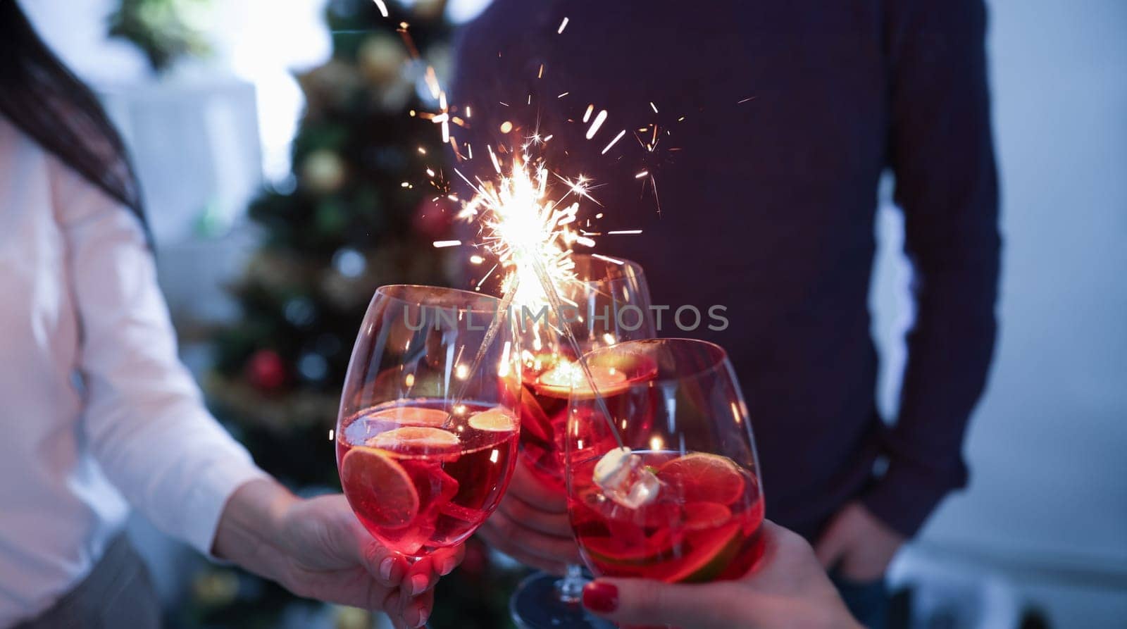 Group of people clinking glasses with alcoholic cocktail and sparklers closeup. New year and christmas carp celebrations concept