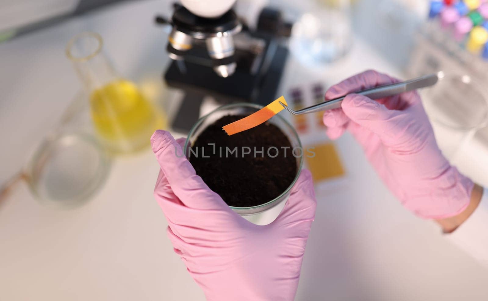 Scientist chemist checking soil acidity using litmus paper in laboratory closeup. Fertilizer production concept