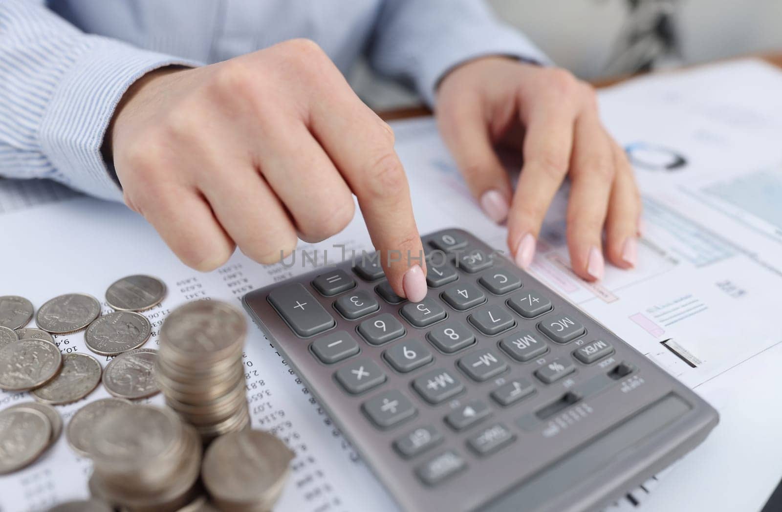 Woman counting on calculator at table with documents and coins closeup. Payment of taxes concept