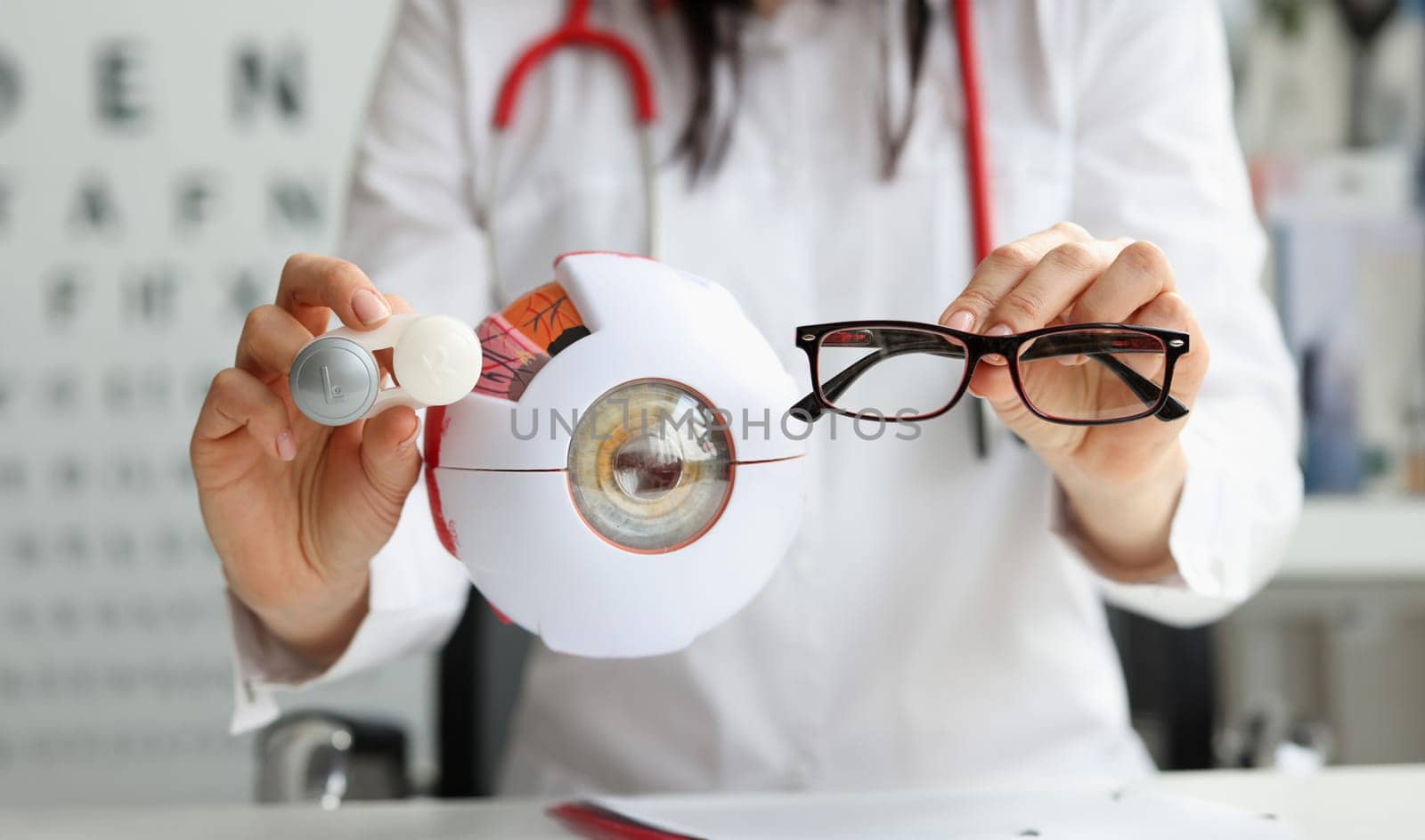 Ophthalmologist doctor holding eyeglasses and lenses near artificial model of eye closeup. Vision correction concept