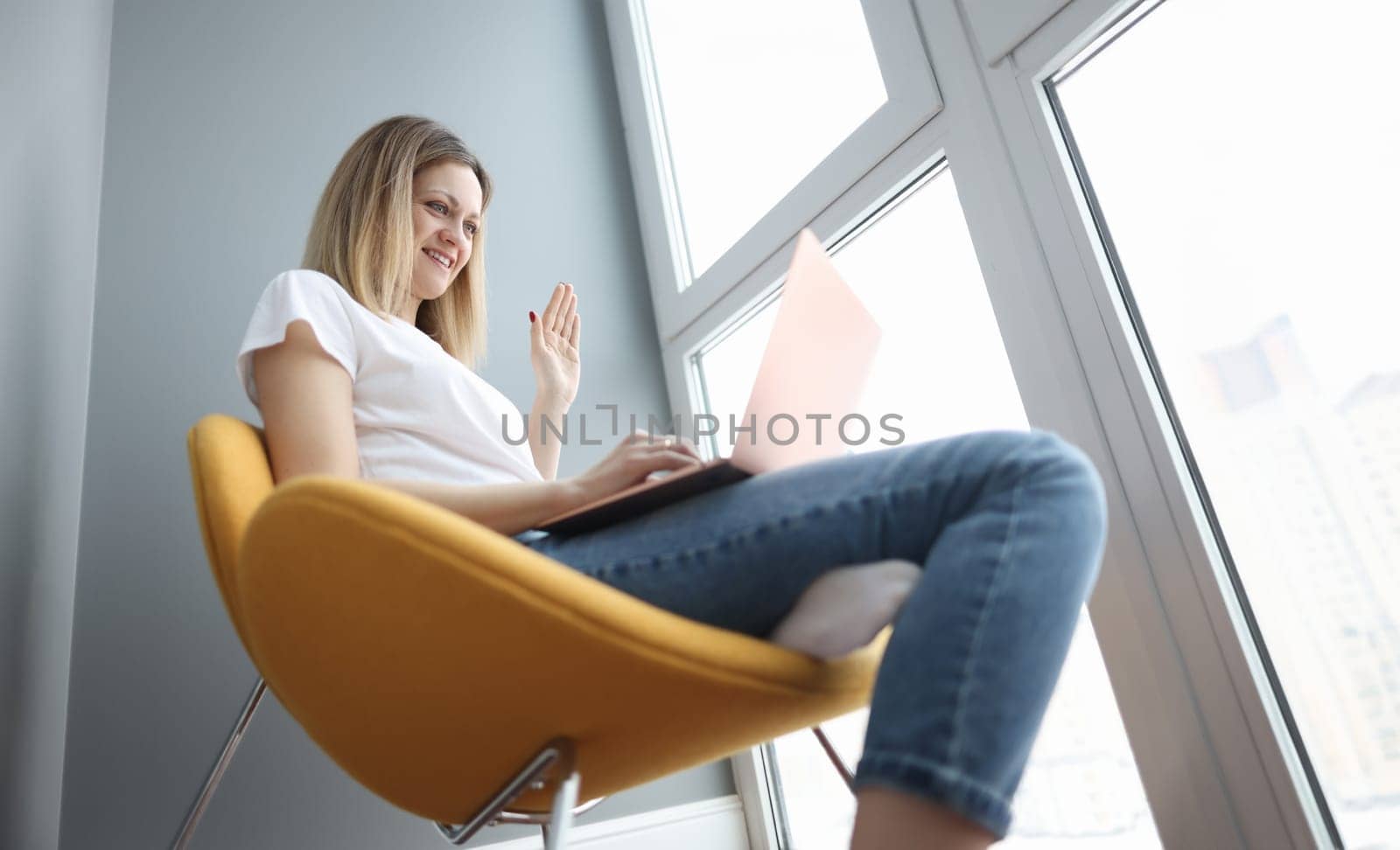 Woman waving hand at laptop screen at home. Self isolation during covid19 pandemic concept