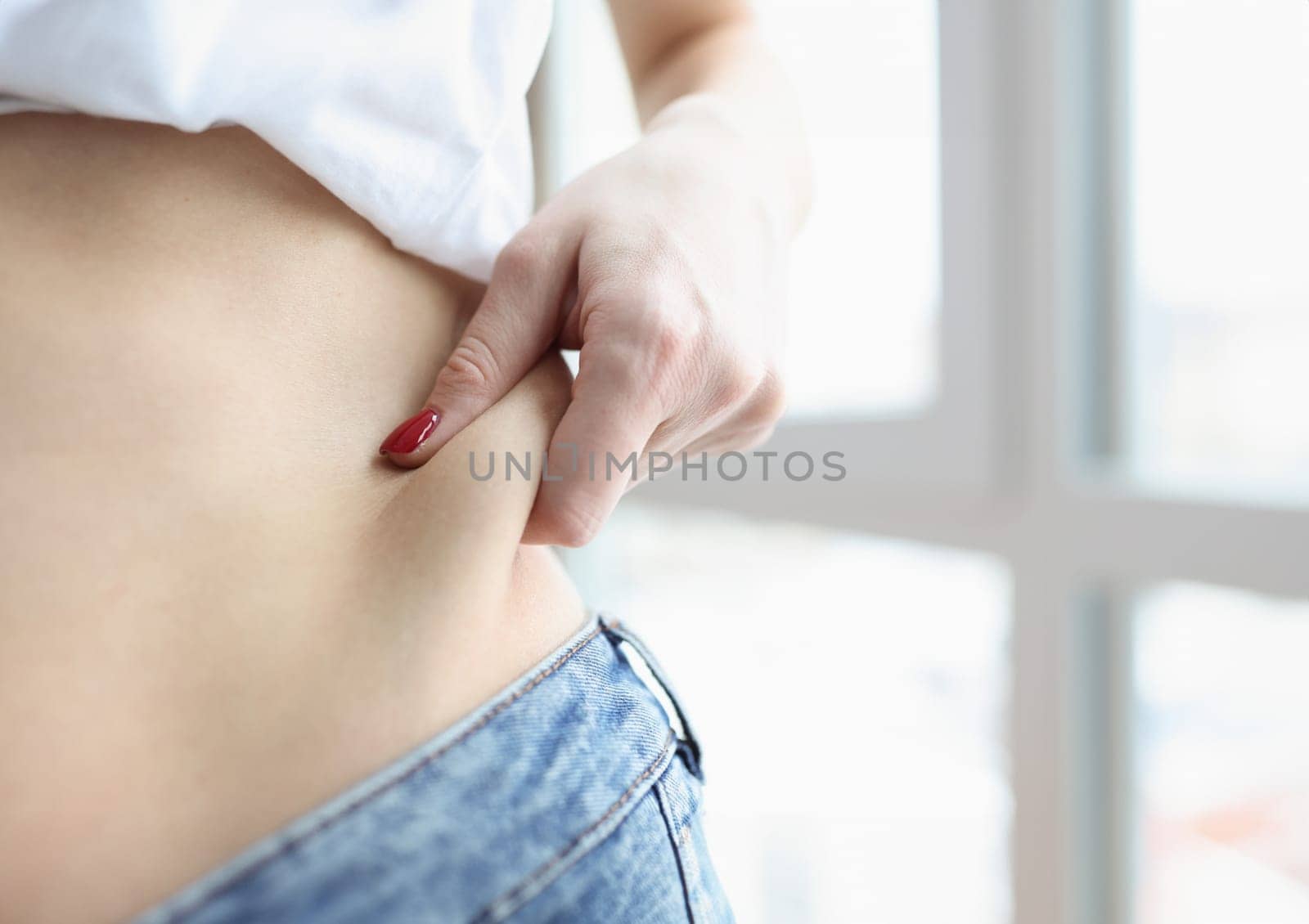 Woman pulling off fold of fat at her waist closeup. Liposuction body shaping concept