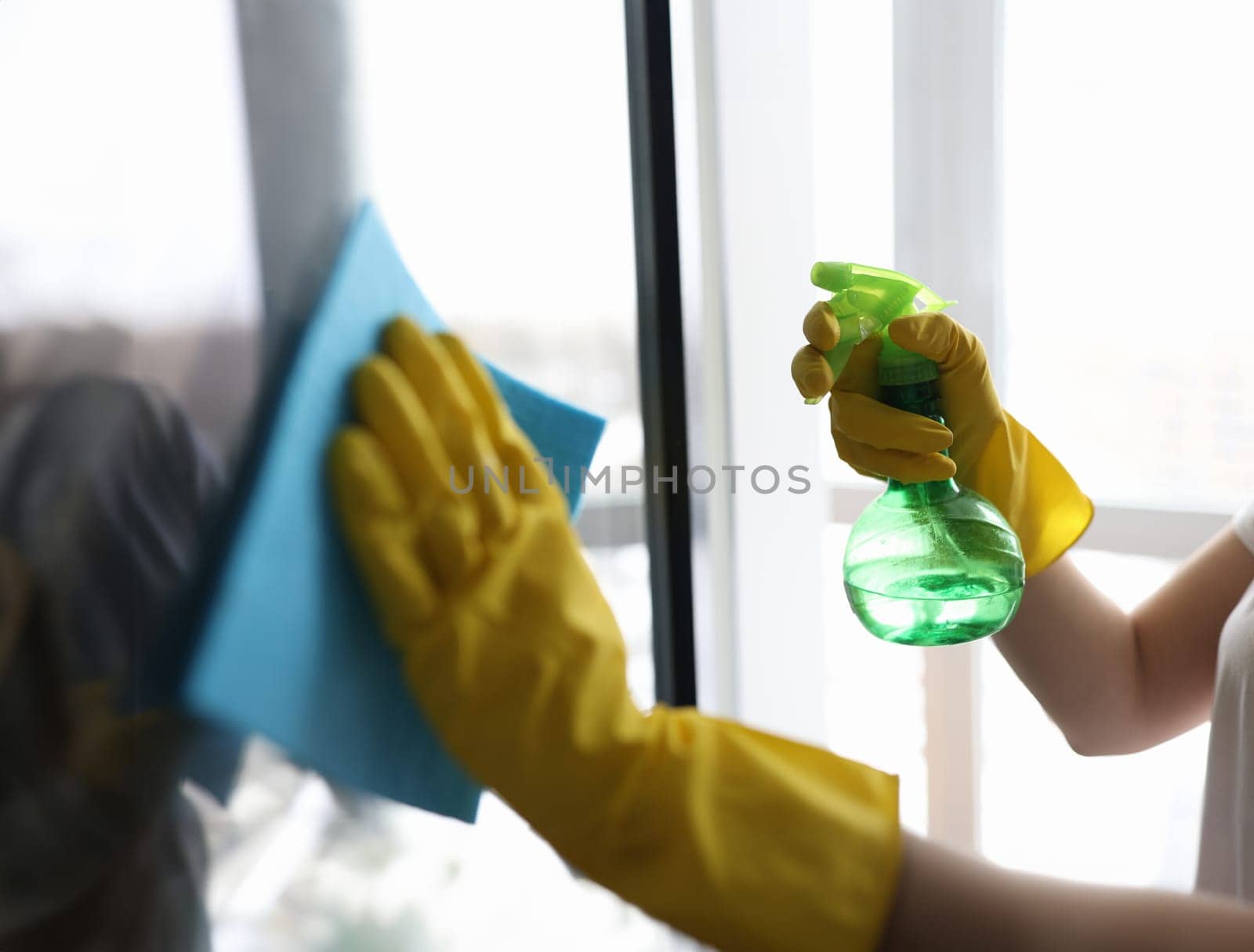 Housekeeper in gloves washing window with napkin closeup. Cleaning of apartments and offices concept
