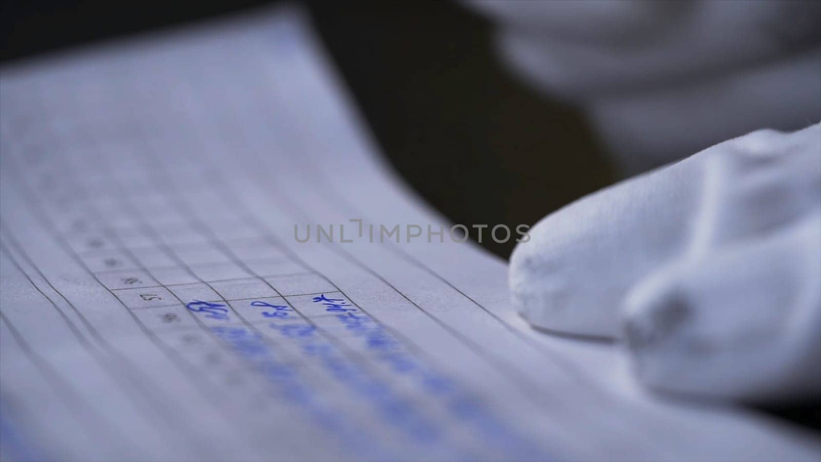 Side view of a hand making notes in a logbook. Close up of hands in white gloves writing data in the notebook with a pen on black background.