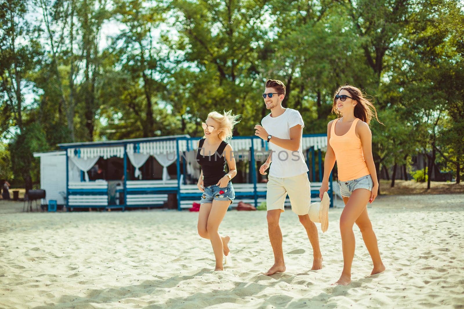 Young funny guys in sunglasses on the beach. Friends together. Summer bar is on background.