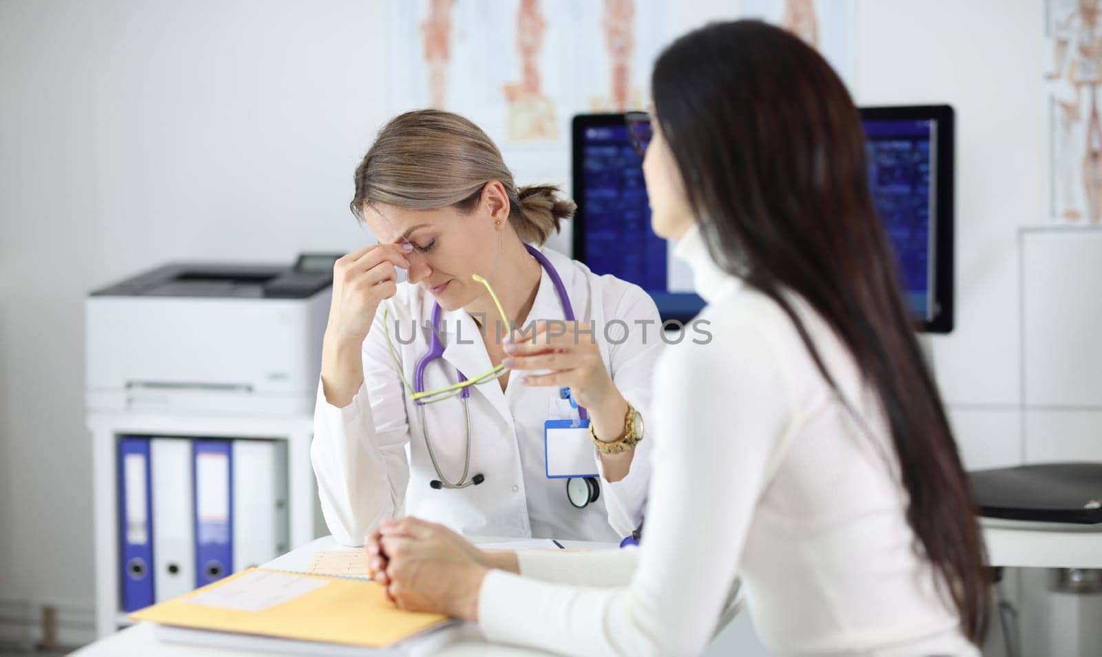 Tired doctor taking off glasses in front of patient in clinic. Medical bad news concept