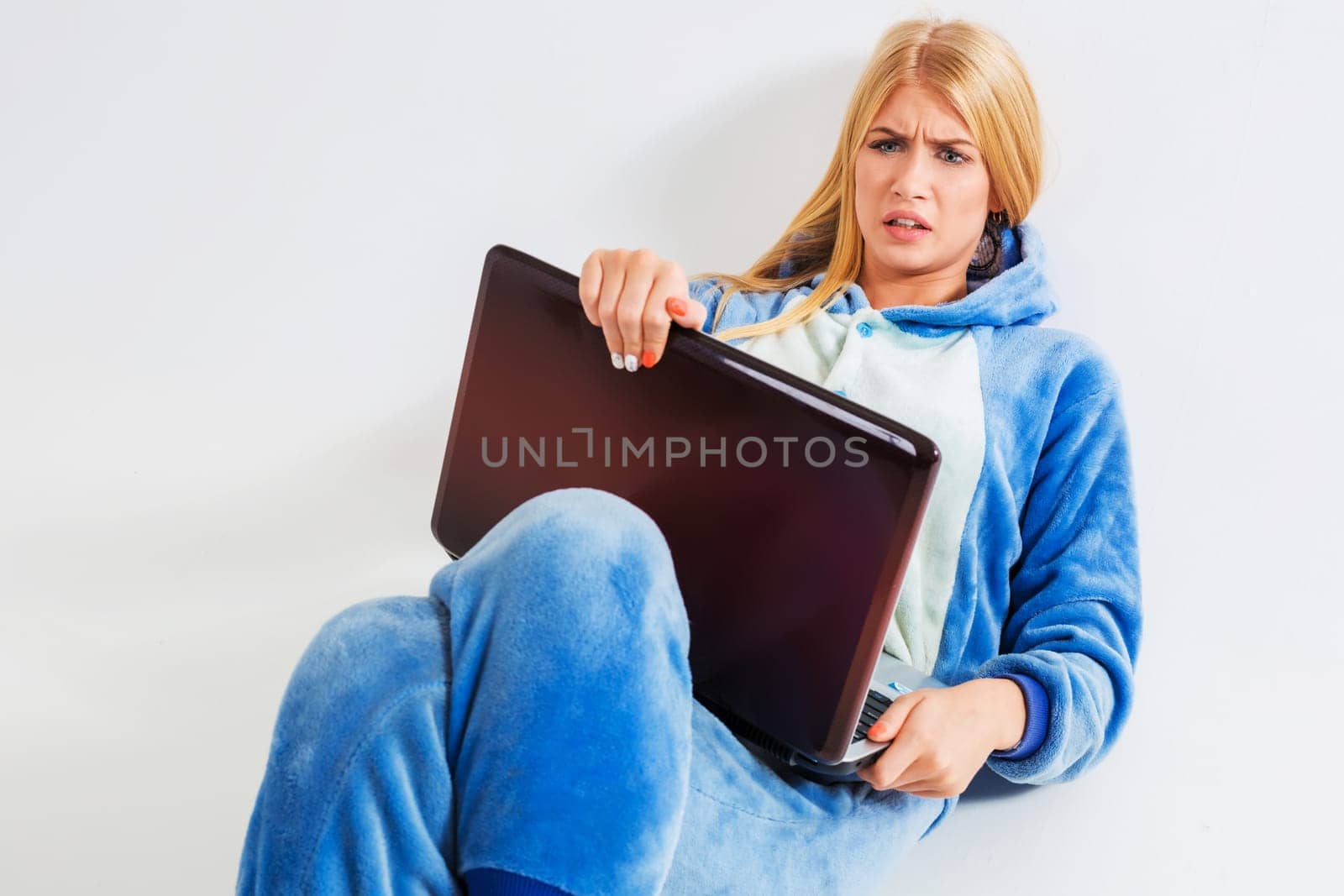 girl in pajamas with a laptop lying on the floor. studying or doing online shopping. work from home. annoyed, surprised, frowning
