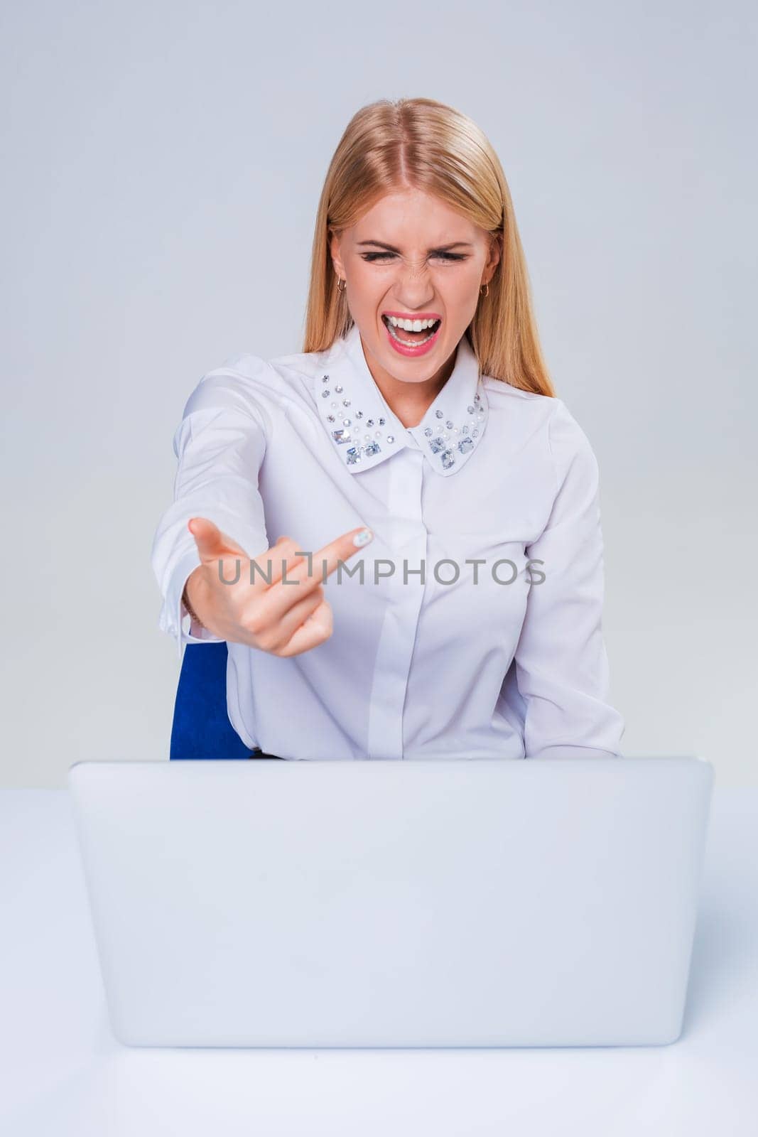 Young businesswoman working at laptop computer. hiding behind the monitor. frustrated, spiteful woman in shock showing middle finger