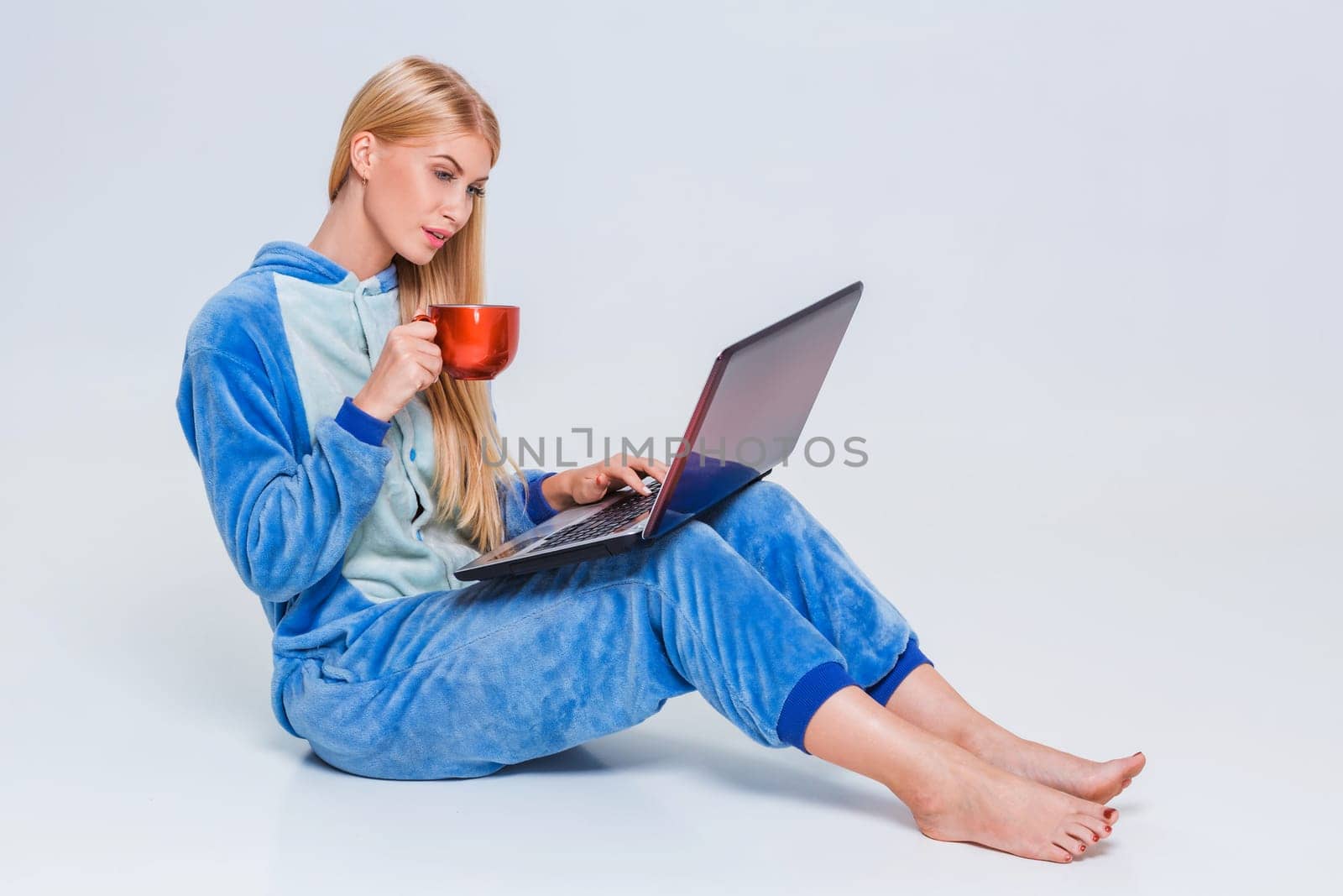 girl in pajamas with a laptop lying on the floor. studying or doing online shopping. work from home. Satisfied and smiling. drinking coffee or tea