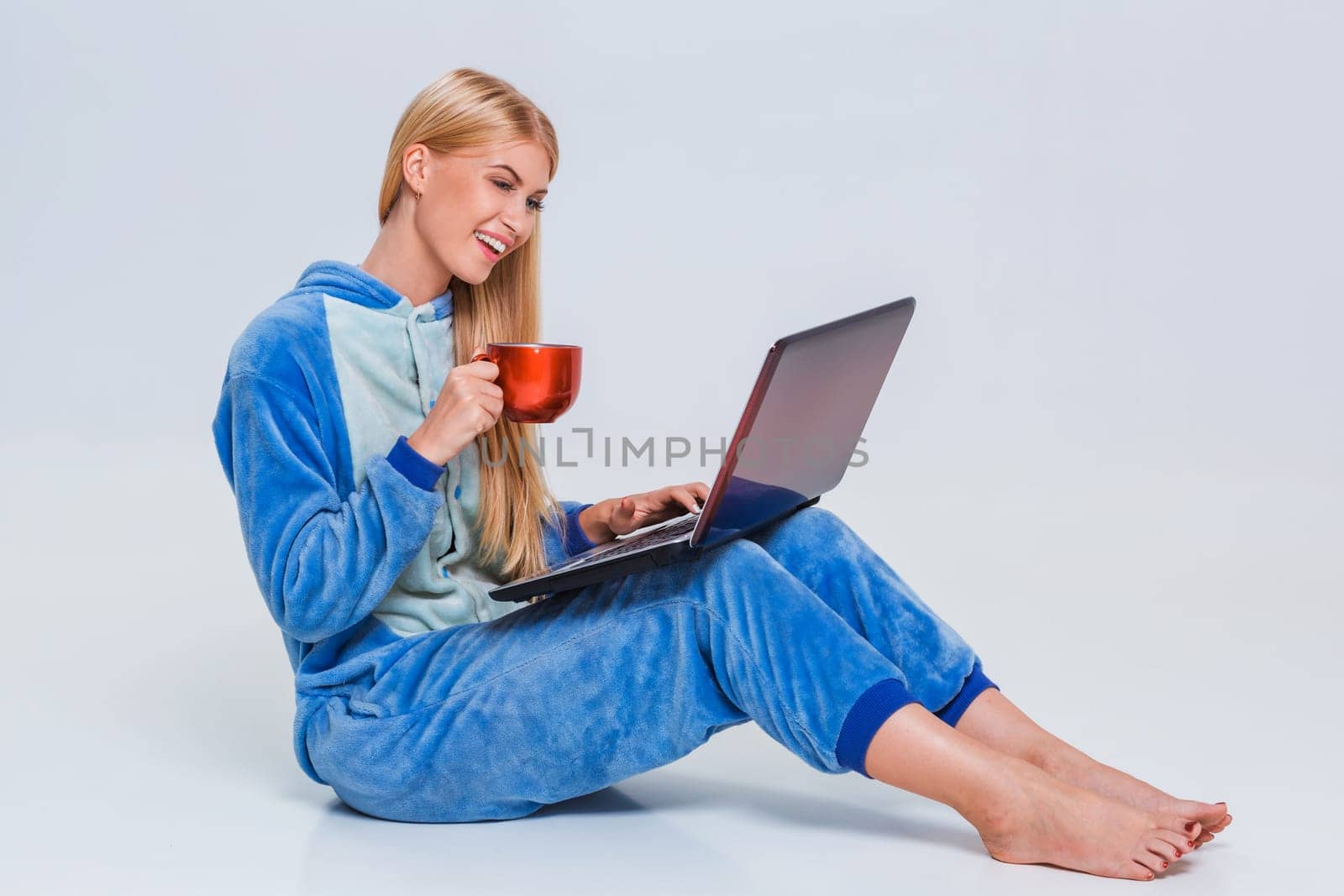 girl in pajamas with a laptop lying on the floor. studying or doing online shopping. work from home. Satisfied and smiling. drinking coffee or tea