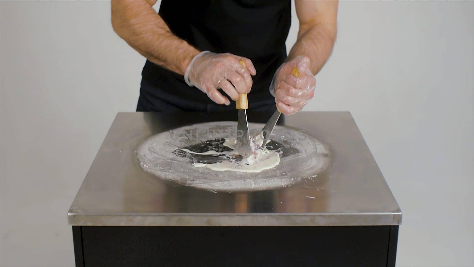 Cooking natural fruit ice cream in Thai style. Clip. Making ice cream rolls with passion fruit on cold plate. Making ice cream rolls on cold plate. Close up. Thai style stir-fried rolled ice cream being prepared. Exotic hand-made frozen dessert being made on steel plate iced grill