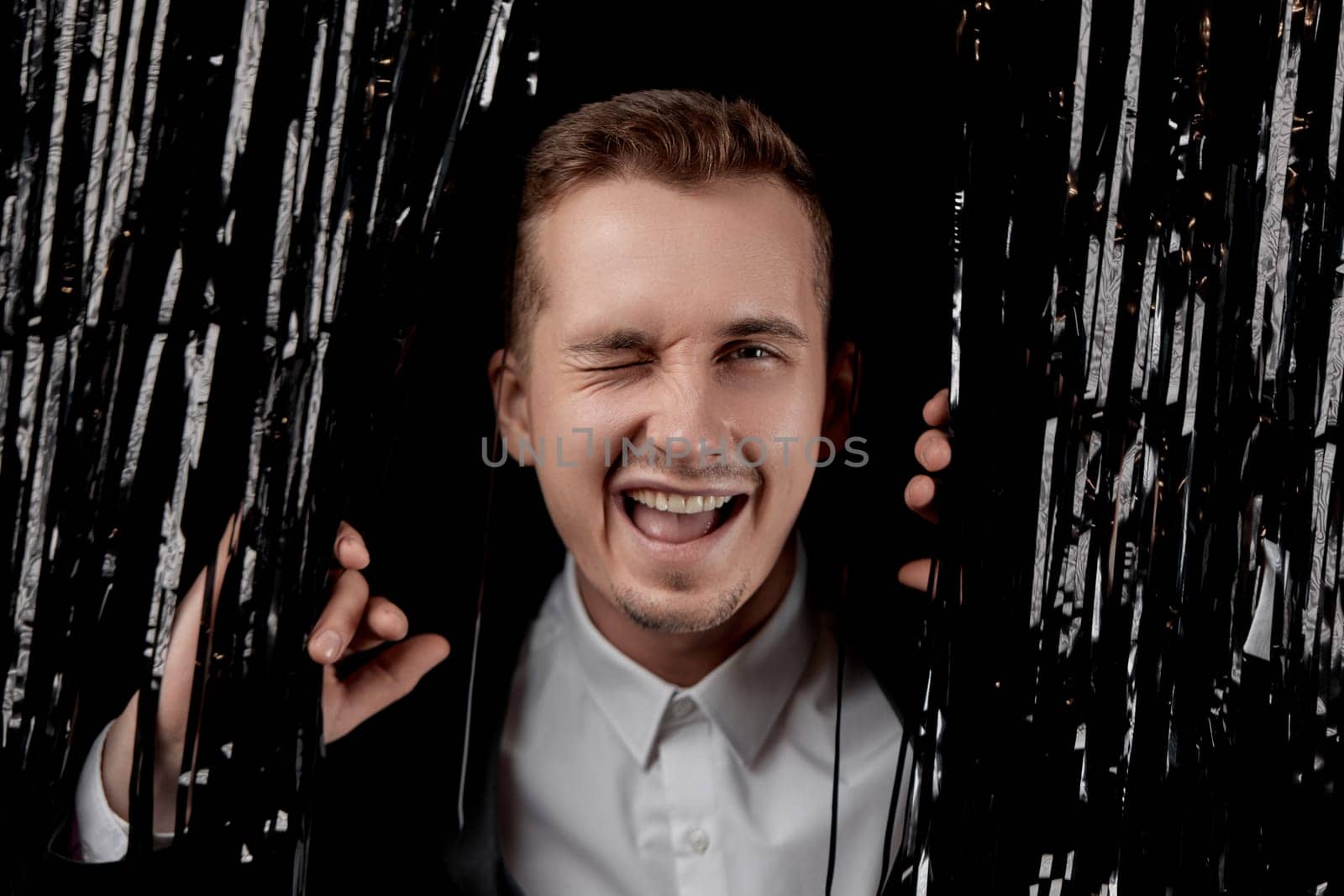 handsome man in black suit winking looking at the camera with happy expression on glitter background.