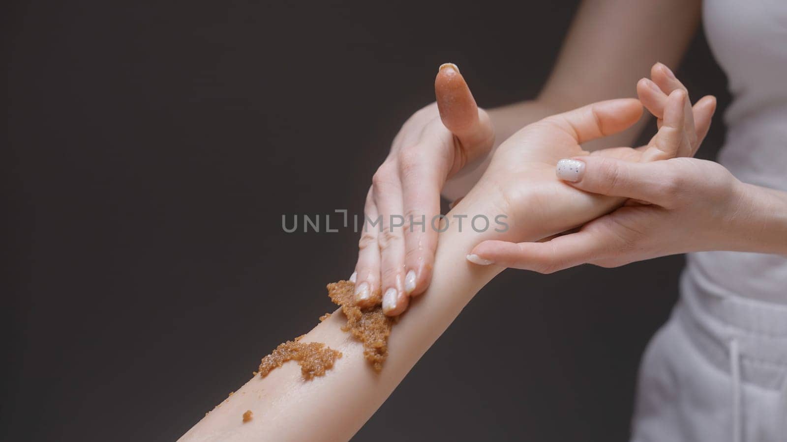 Close-up of masseur rubbing scrub on hand. Action. Gentle movements of masseur on client's hand. Beautiful massage movements and rubbing.